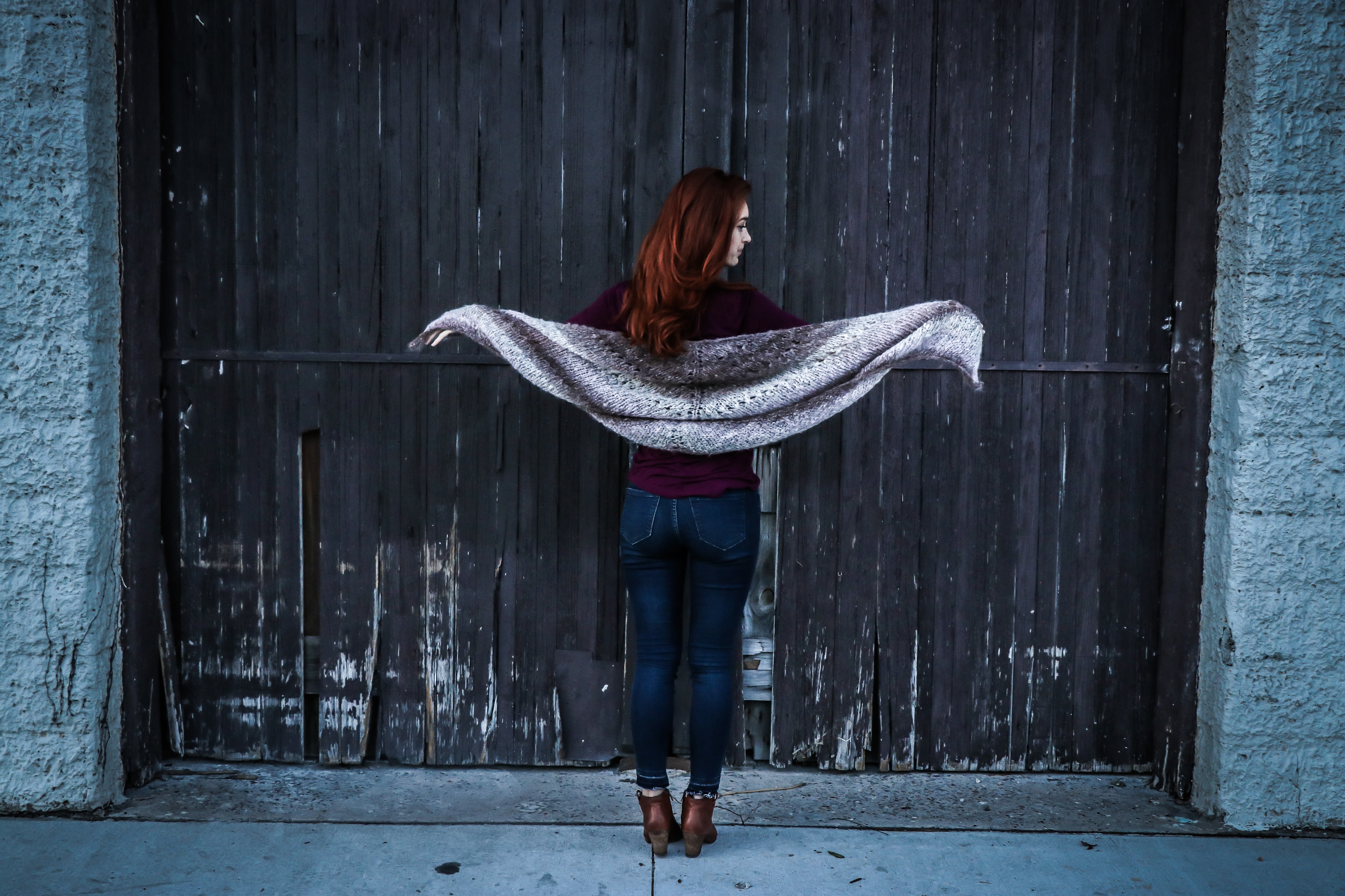 Woman holding gray shawl while spreading her arms infront of brown wooden door photo