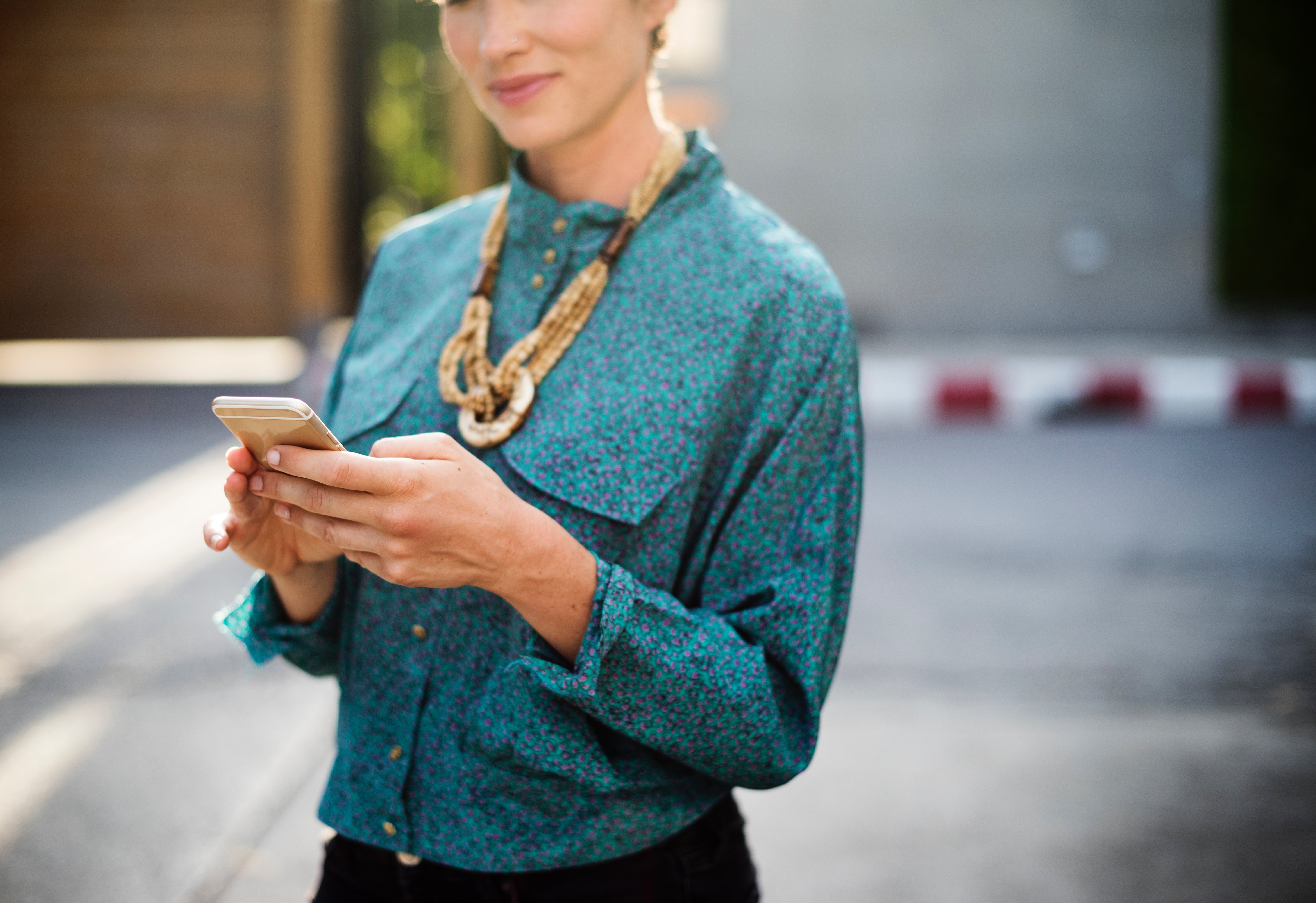 Woman holding iphone wearing long-sleeved shirt and gold necklace photo