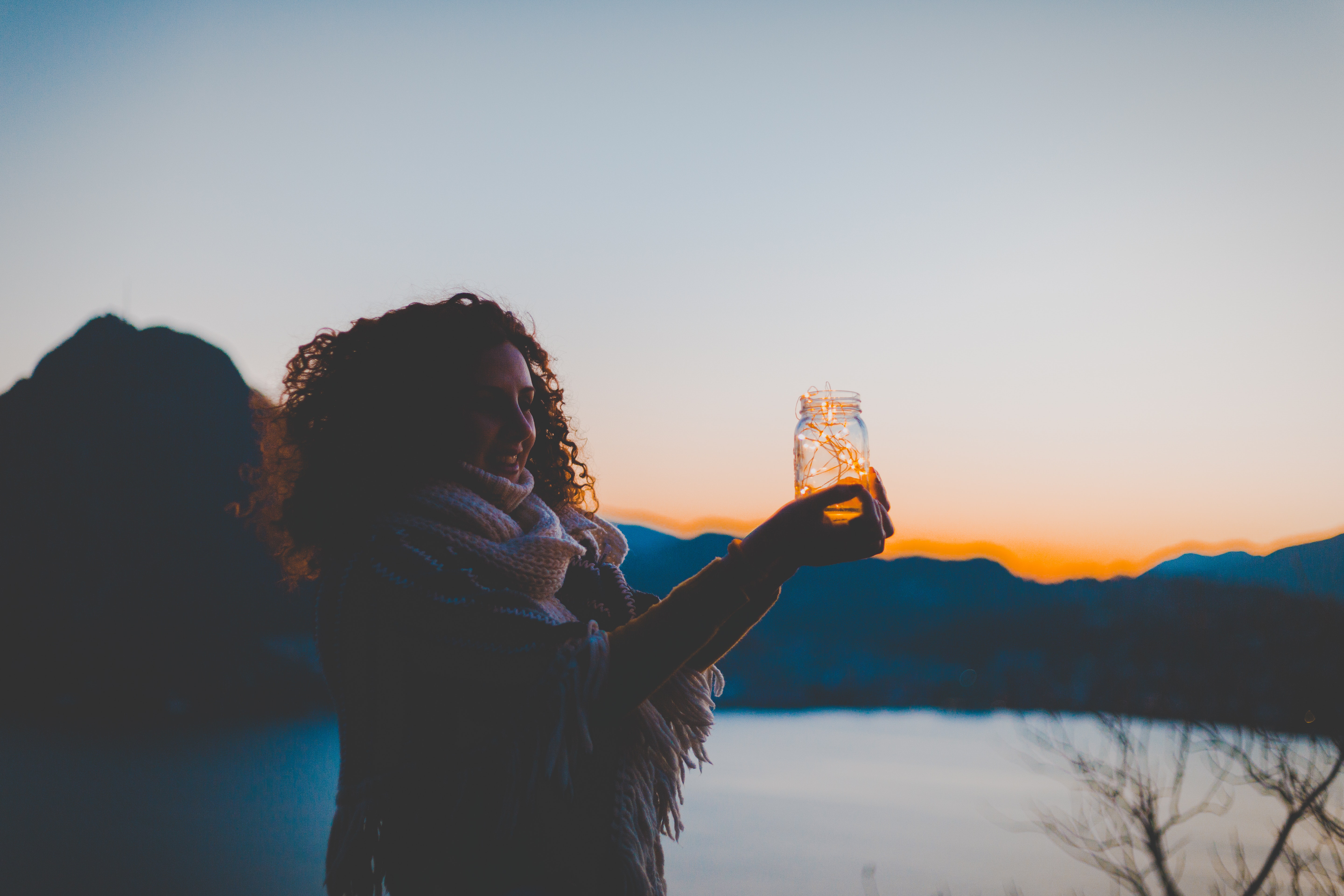 Woman holding mason jar with string light with lake and mountain over view during golden hour photo