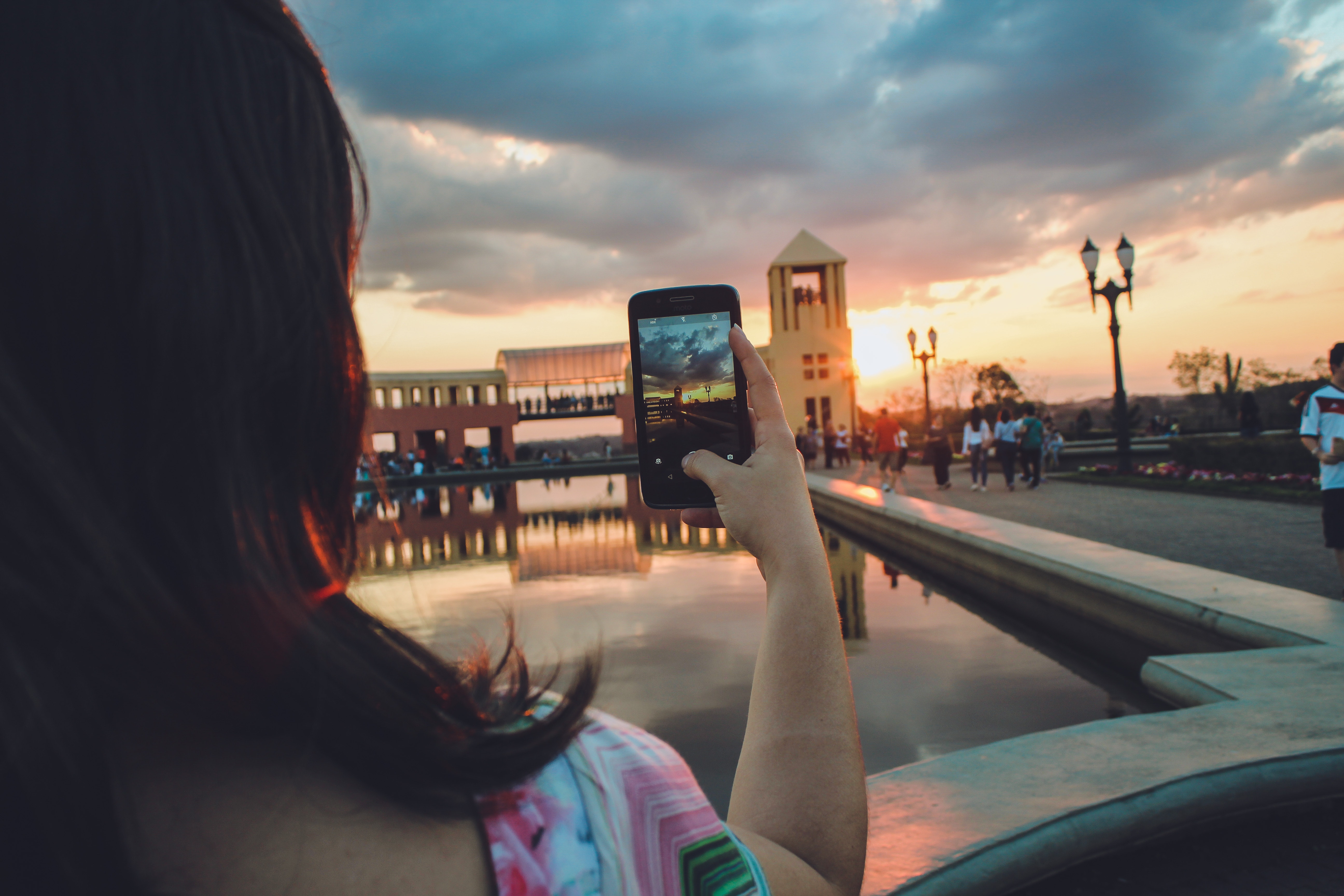 Woman holding smartphone capturing sunset photo