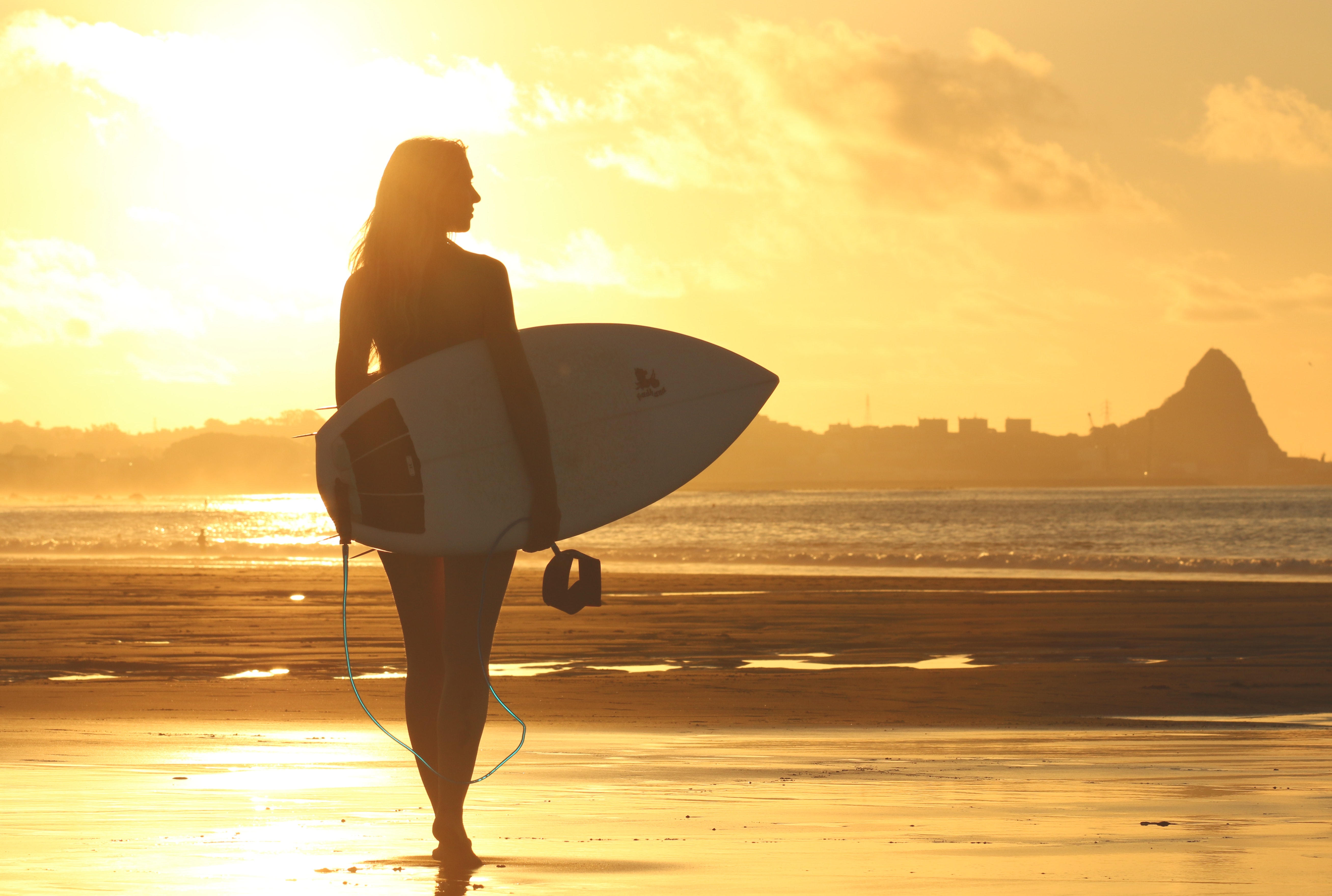 Woman holding surf board standing on shoreline during sunset photo