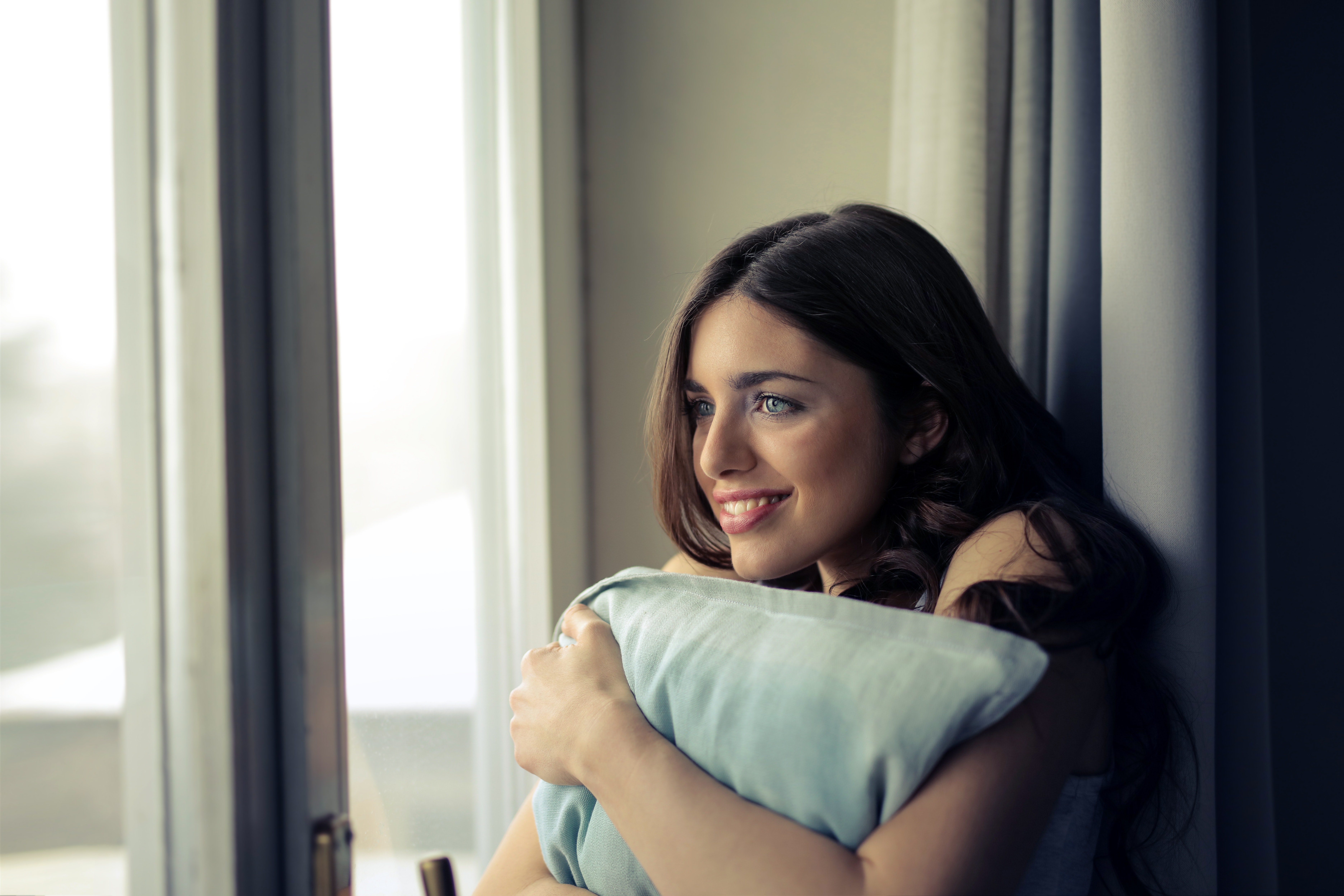 Woman hugging white pillow beside glass door photo