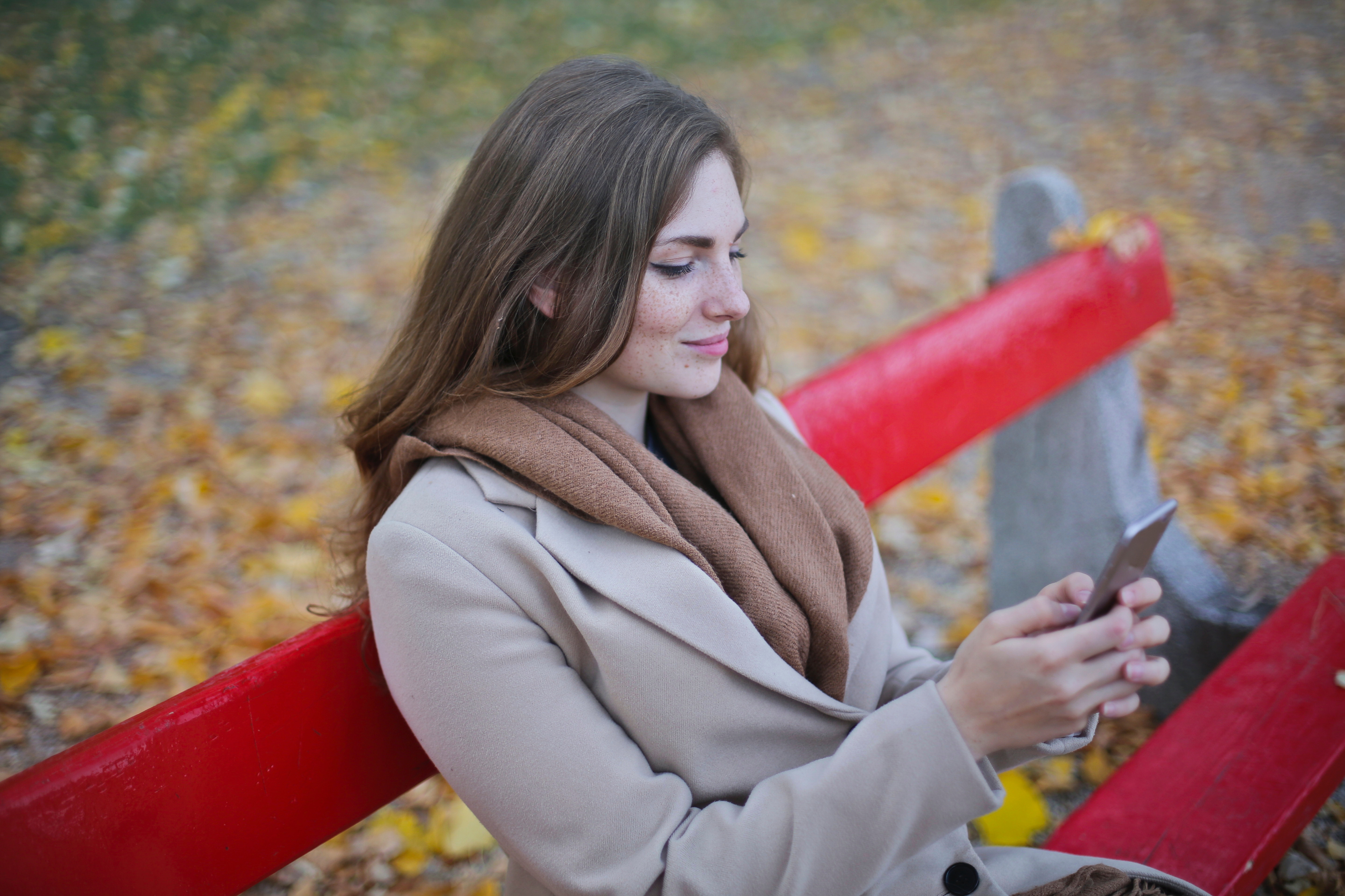 Woman in beige coat holding smartphone sitting on bench photo