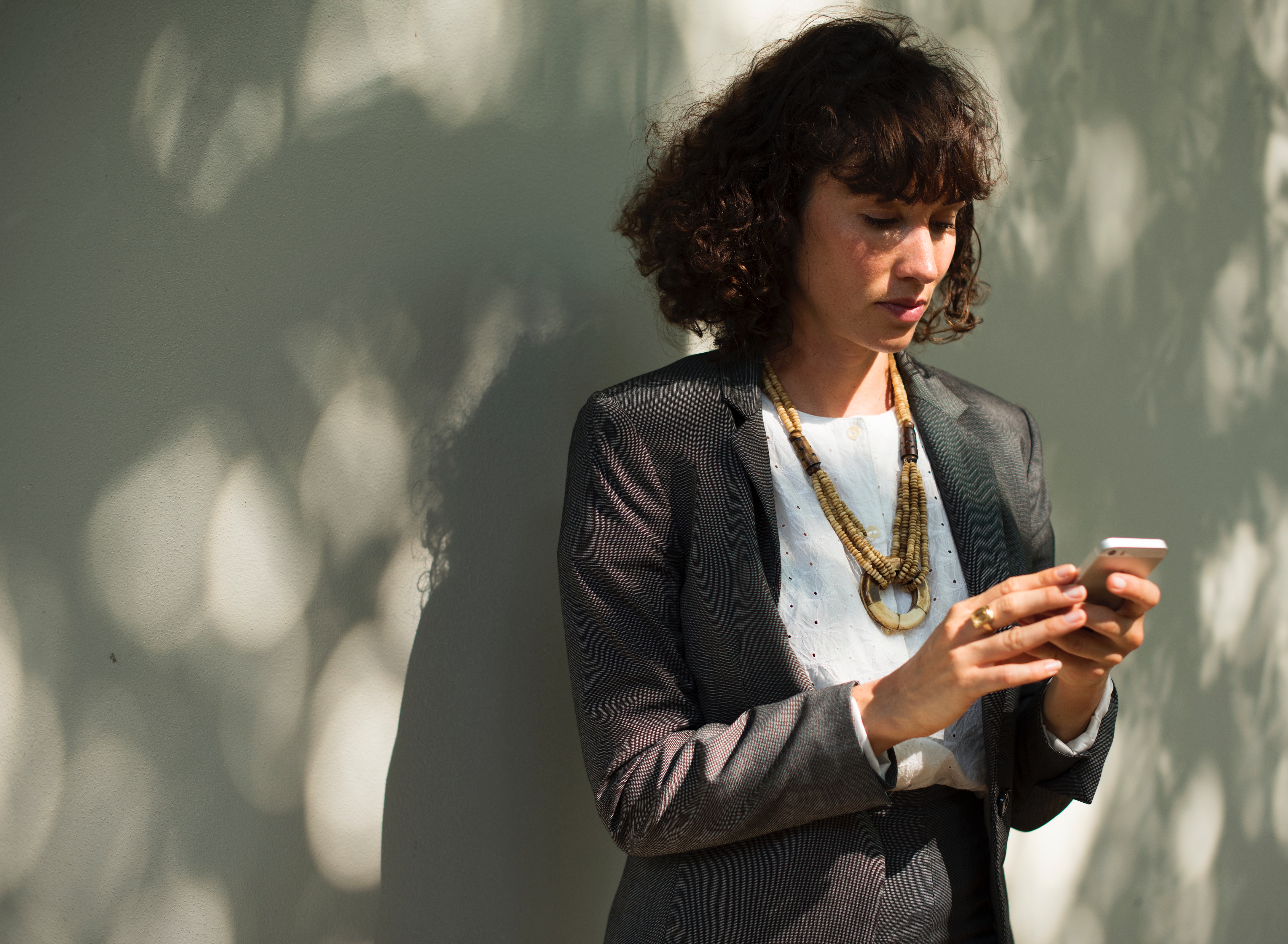 Woman in black blazer holding a smartphone while standing near wall photo