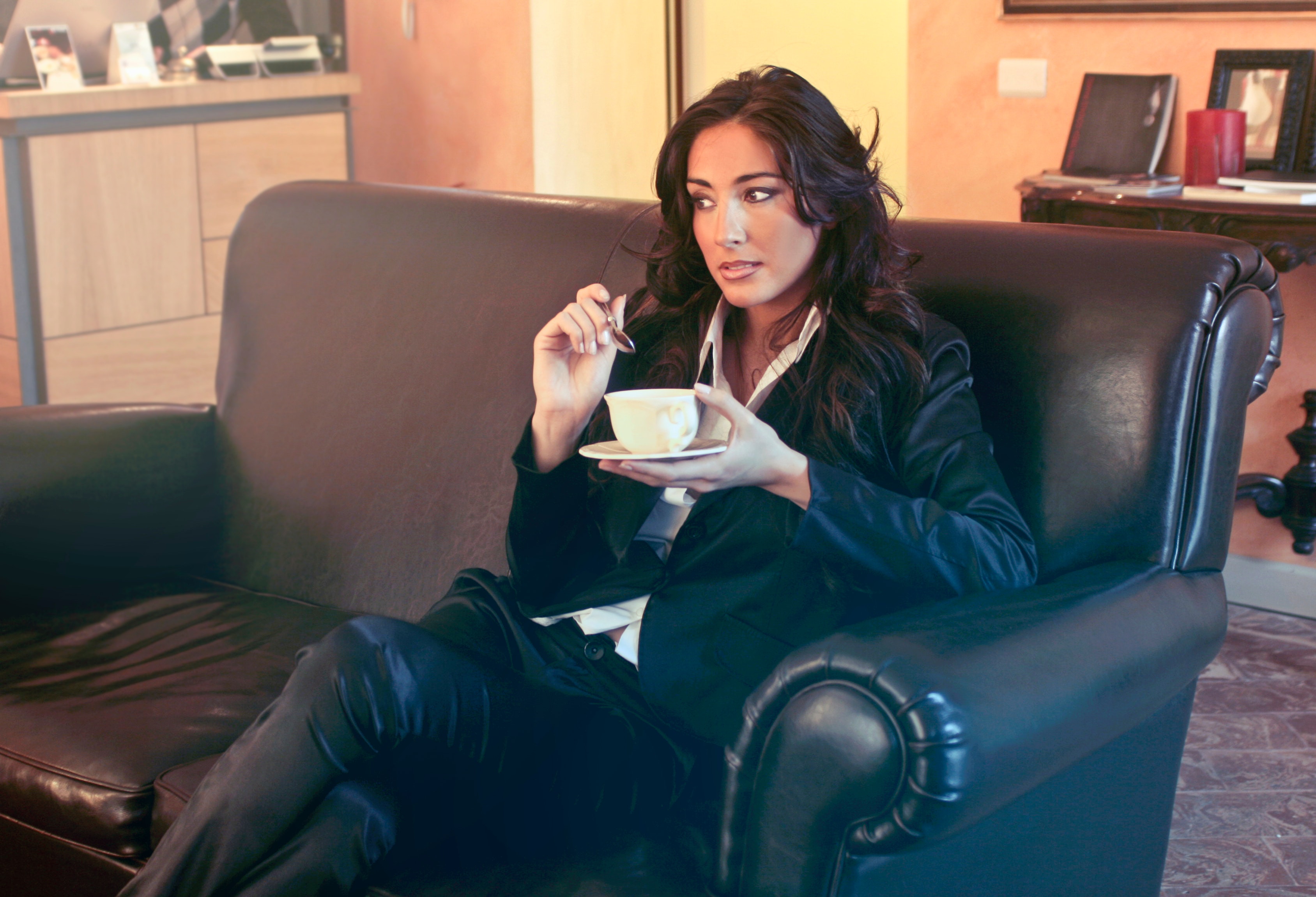 Woman in black blazer holding teacup while sits on black sofa photo