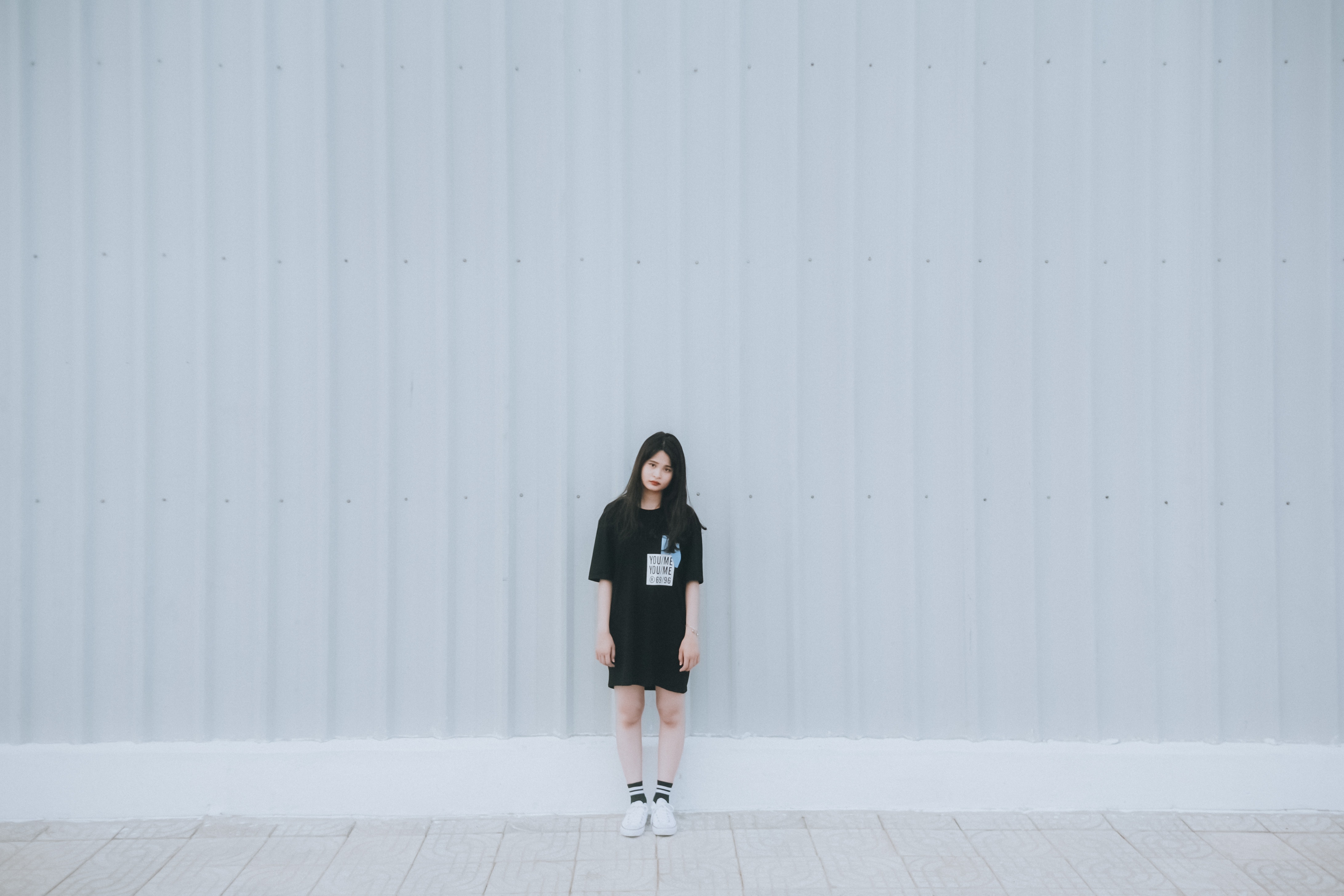 Woman in black elbow sleeve shirt and black shorts standing behind white wall photo