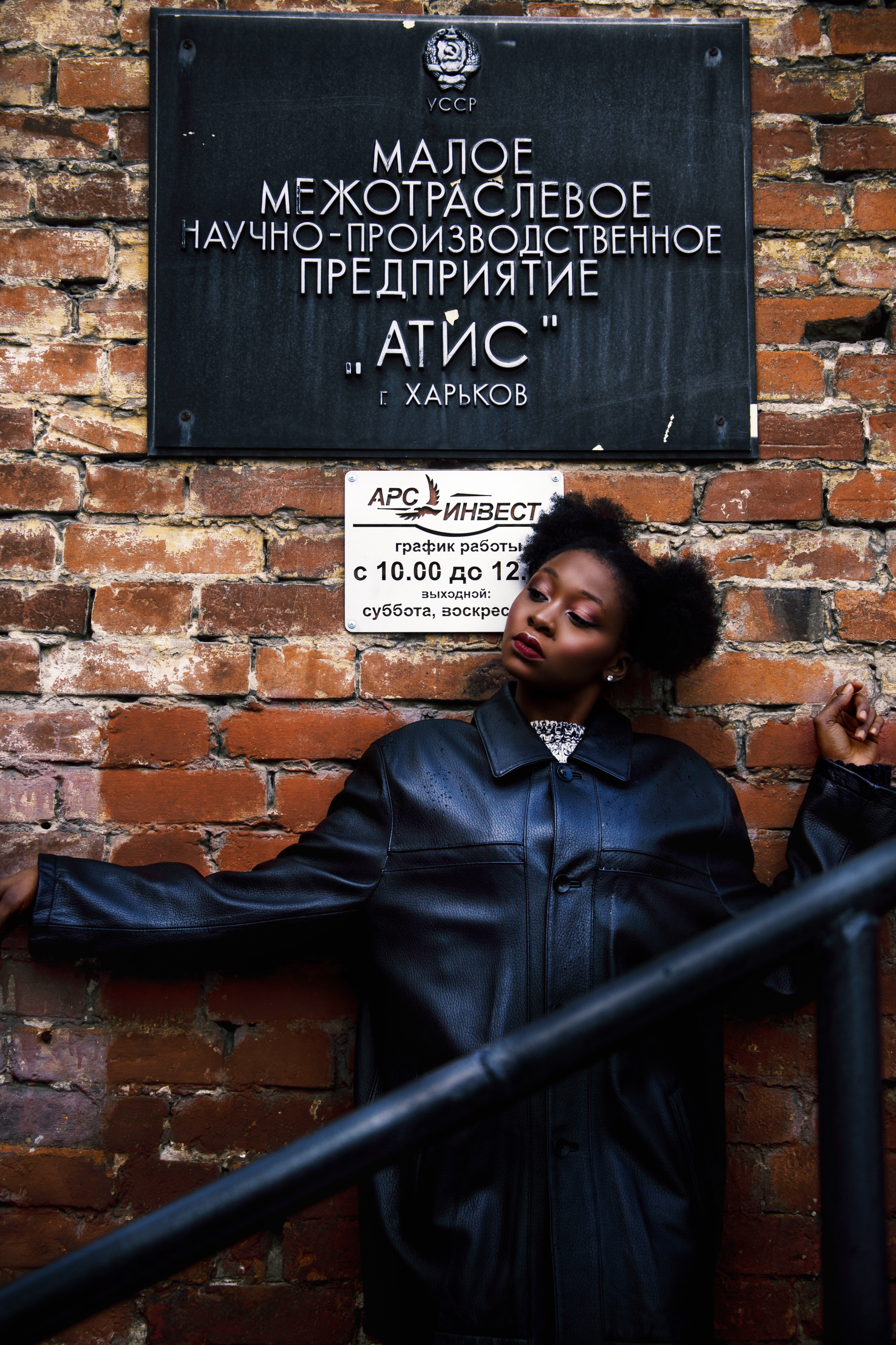 Woman in black leather coat leaning on brick wall photo
