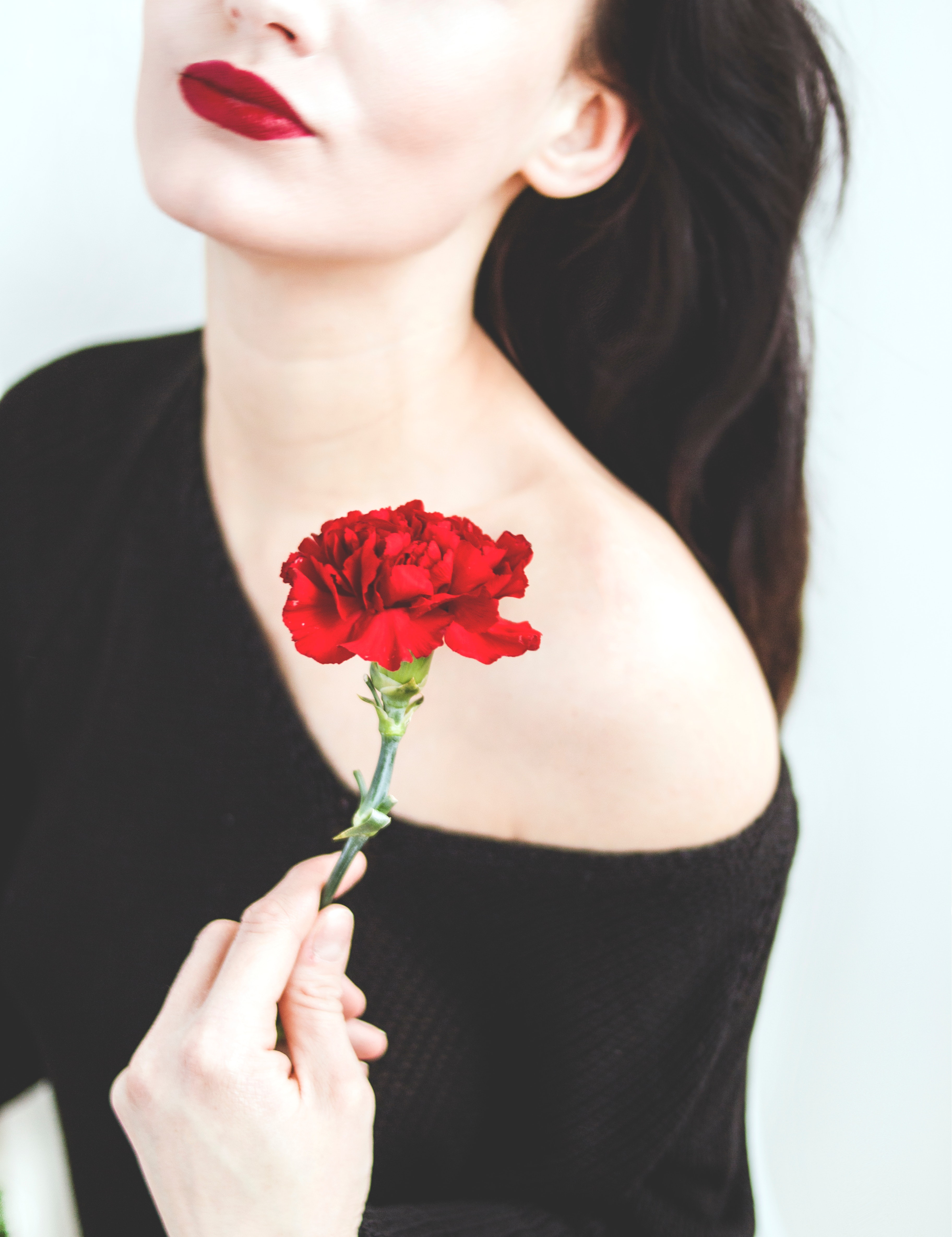 Woman in black one-shoulder top holding red carnation photo