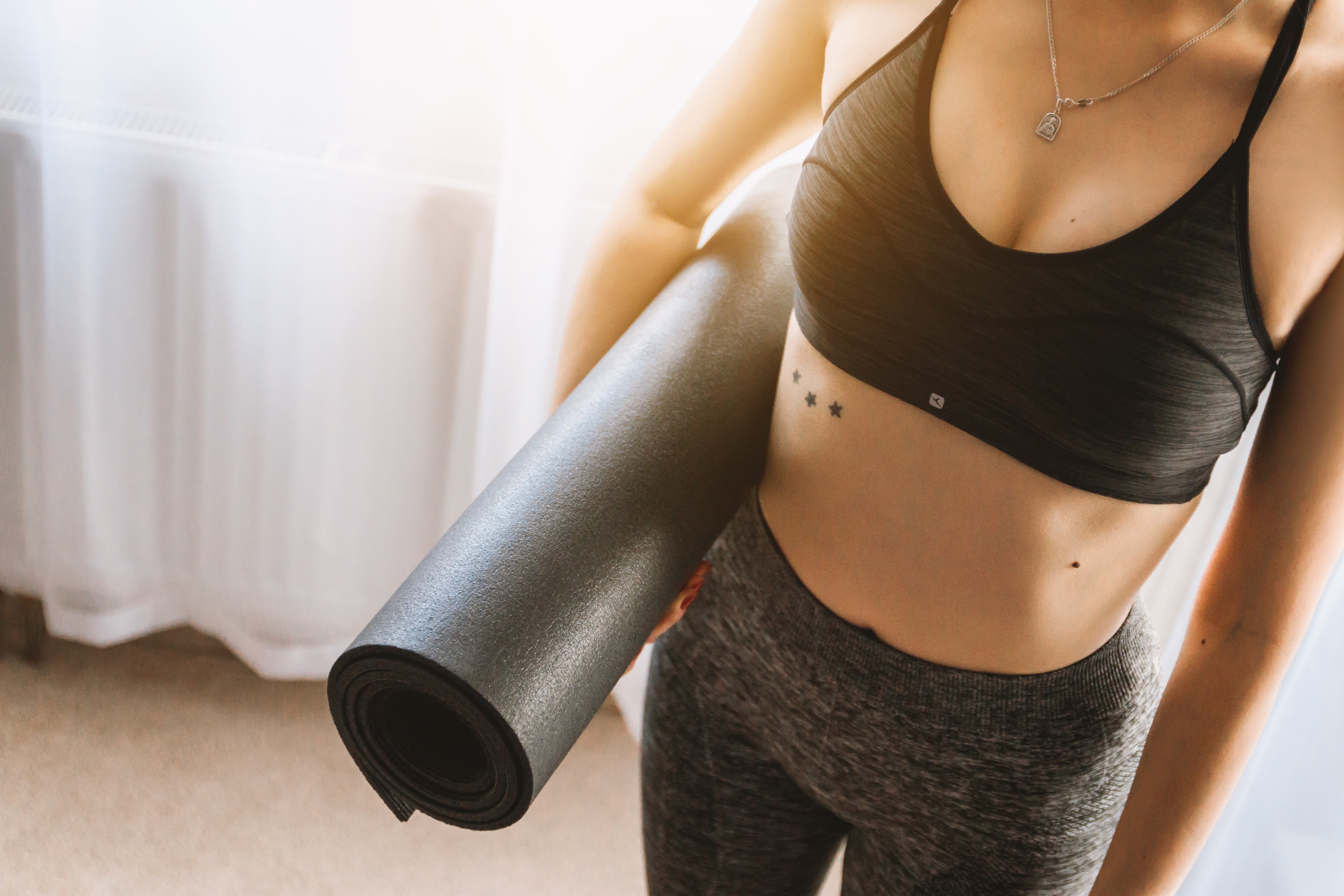 Woman in black sports bra with grey leggings carrying yoga mat photo