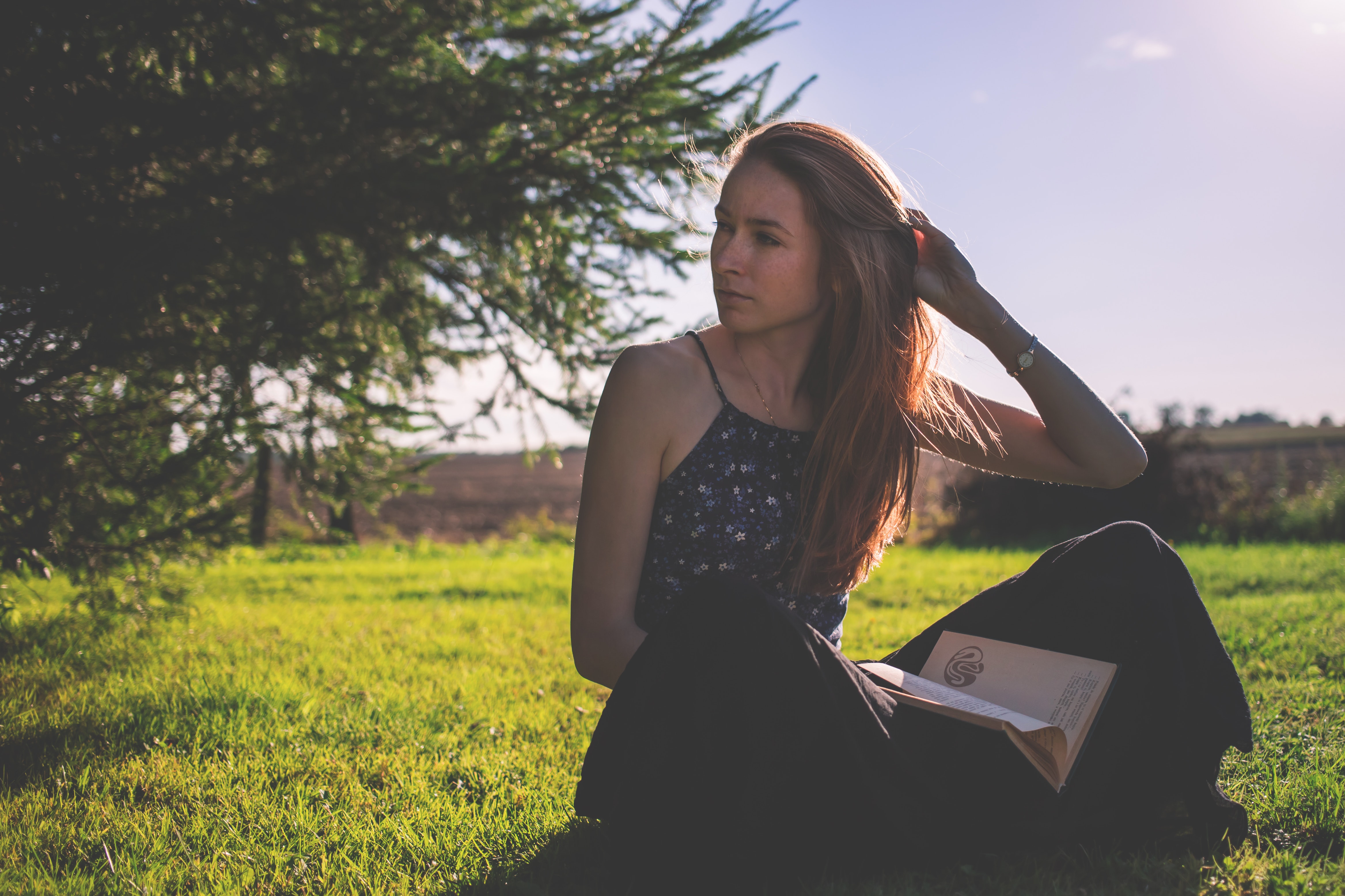 Woman in black tank top and holding brown book sitting on grass under clear sunny sky photo