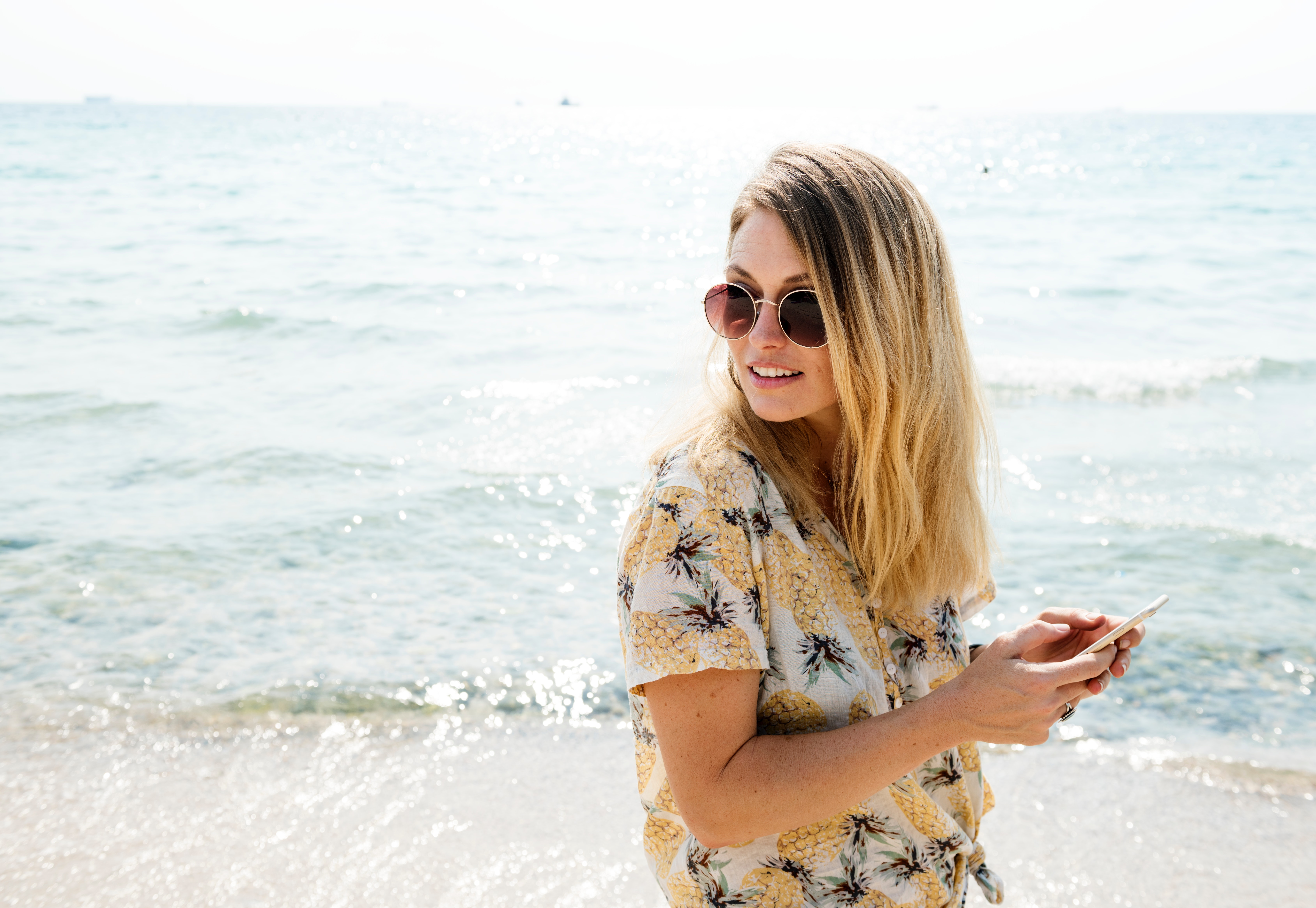 Woman in Black Yellow and White Floral Button-up Shirt Holding Smartphone Wearing Aviator Sunglasses Near Body of Water, Adventure, Tour, Sea, Seashore, HQ Photo