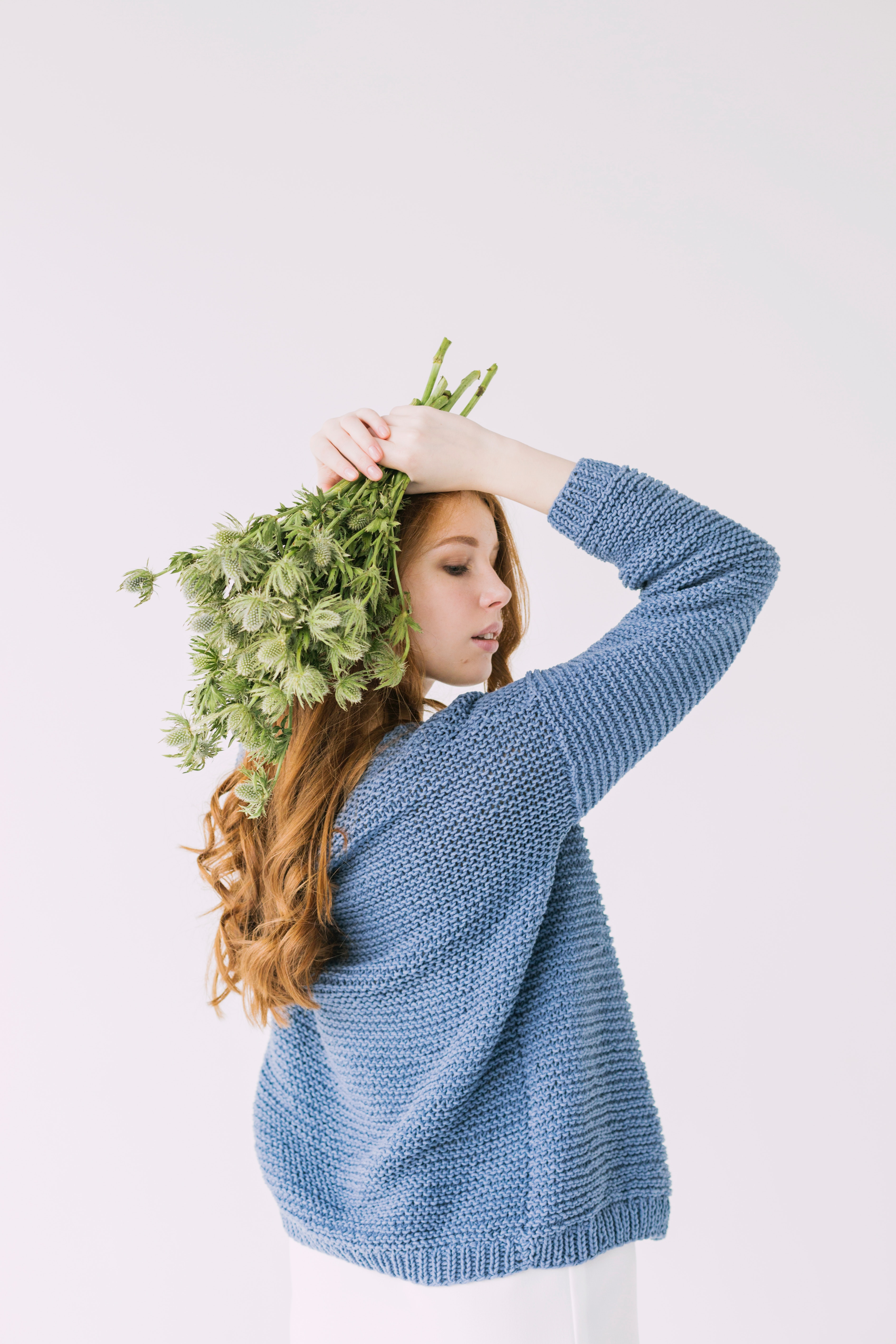 Woman in blue knit cable sweater holding green petaled flowers photo