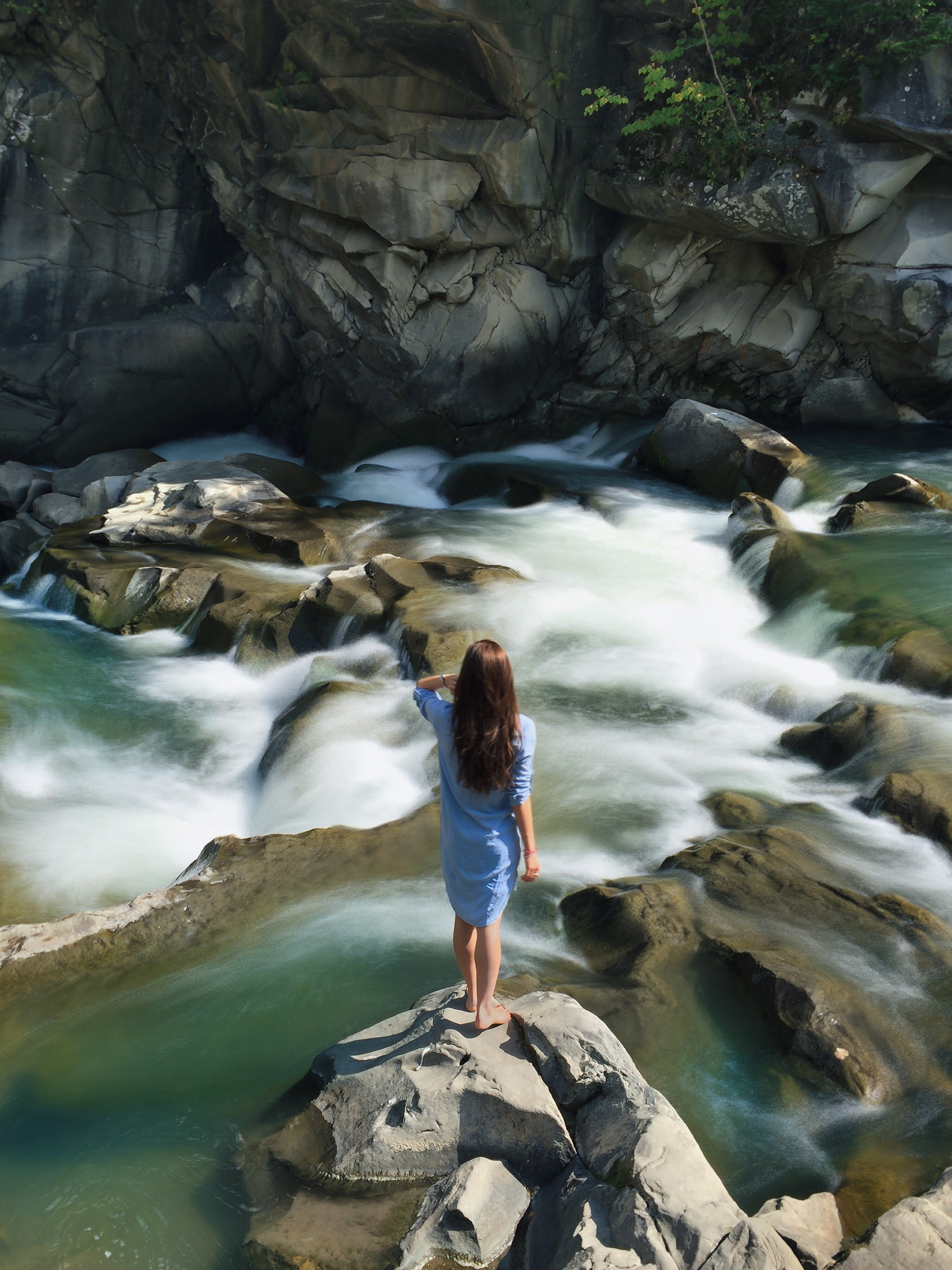 Woman in blue long-sleeved dress standing in middle of rock with raging water photo