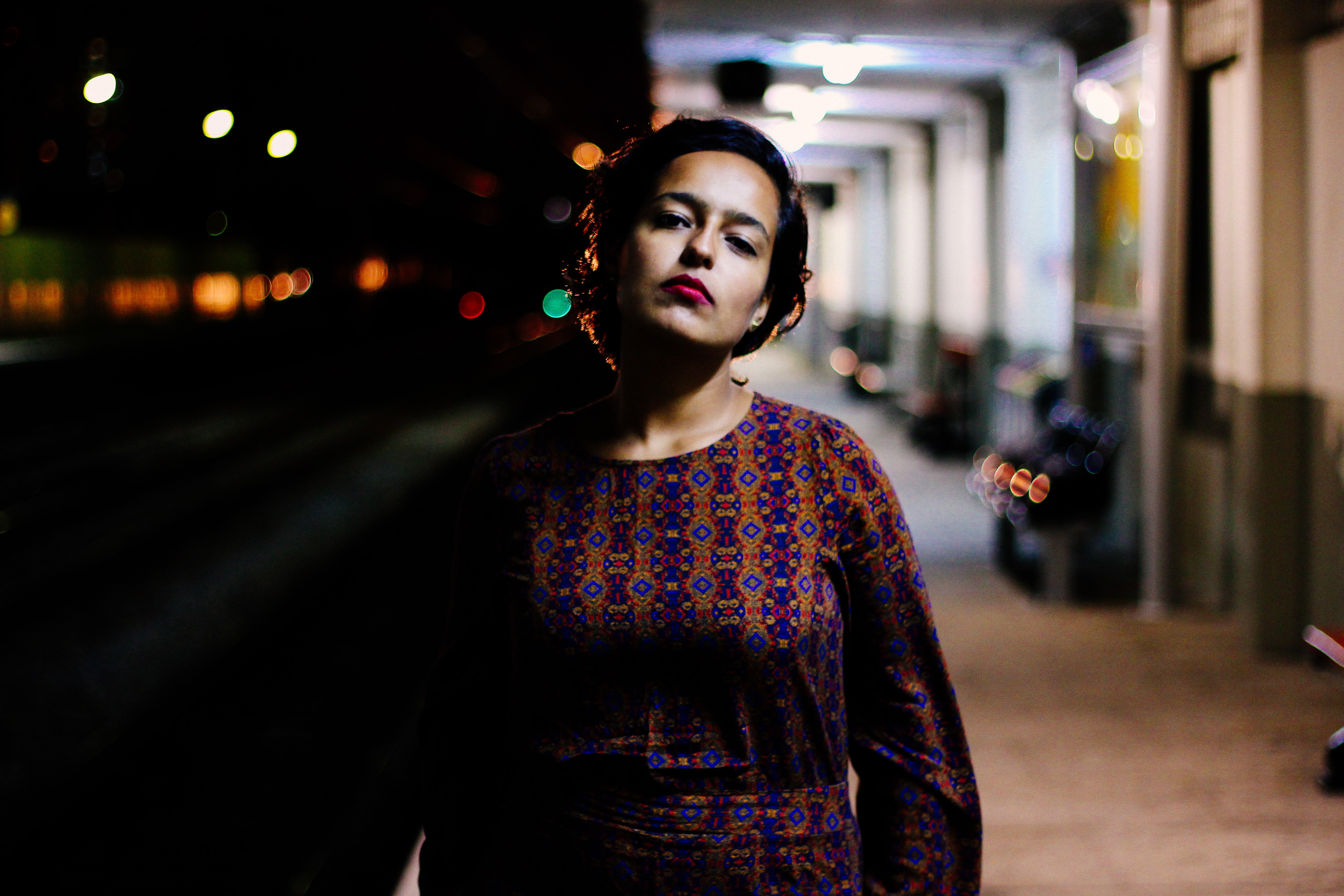 Woman in brown and purple long-sleeved shirt standing outside white building during nighttime photo