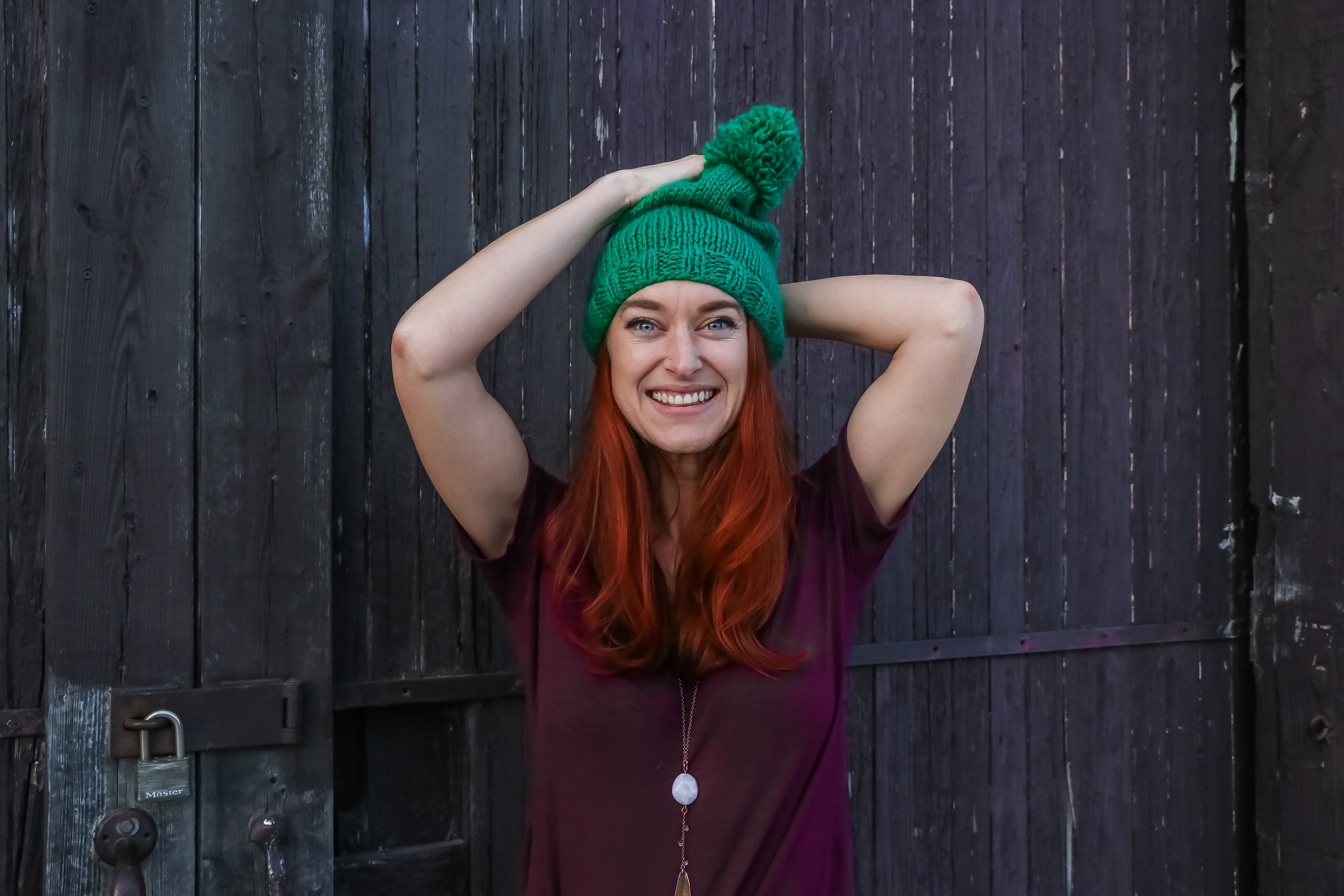 Woman in green bobble cap and purple t-shirt posing near black wooden fence photo