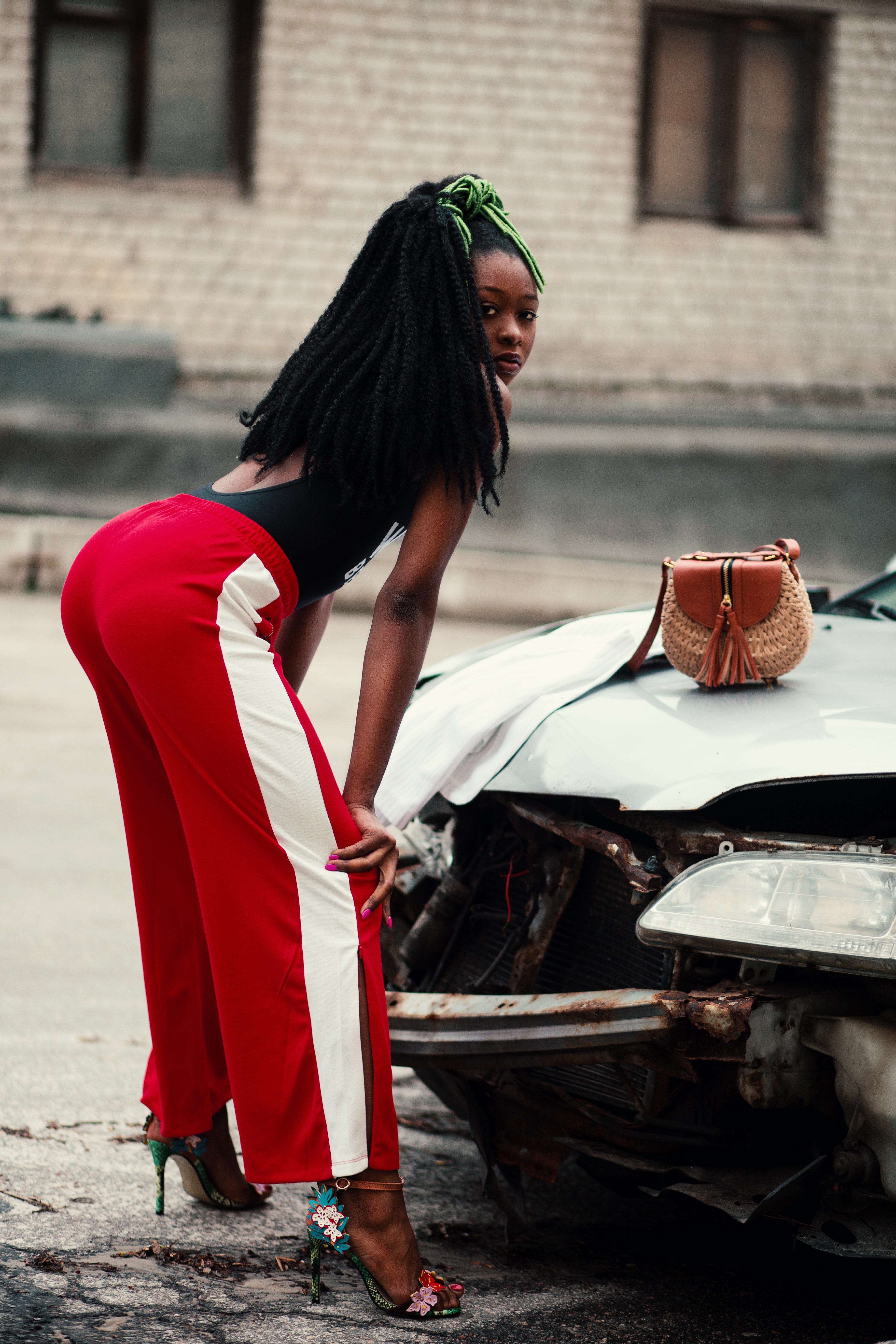 Woman in maroon and white pants leaning in front of broken car photo