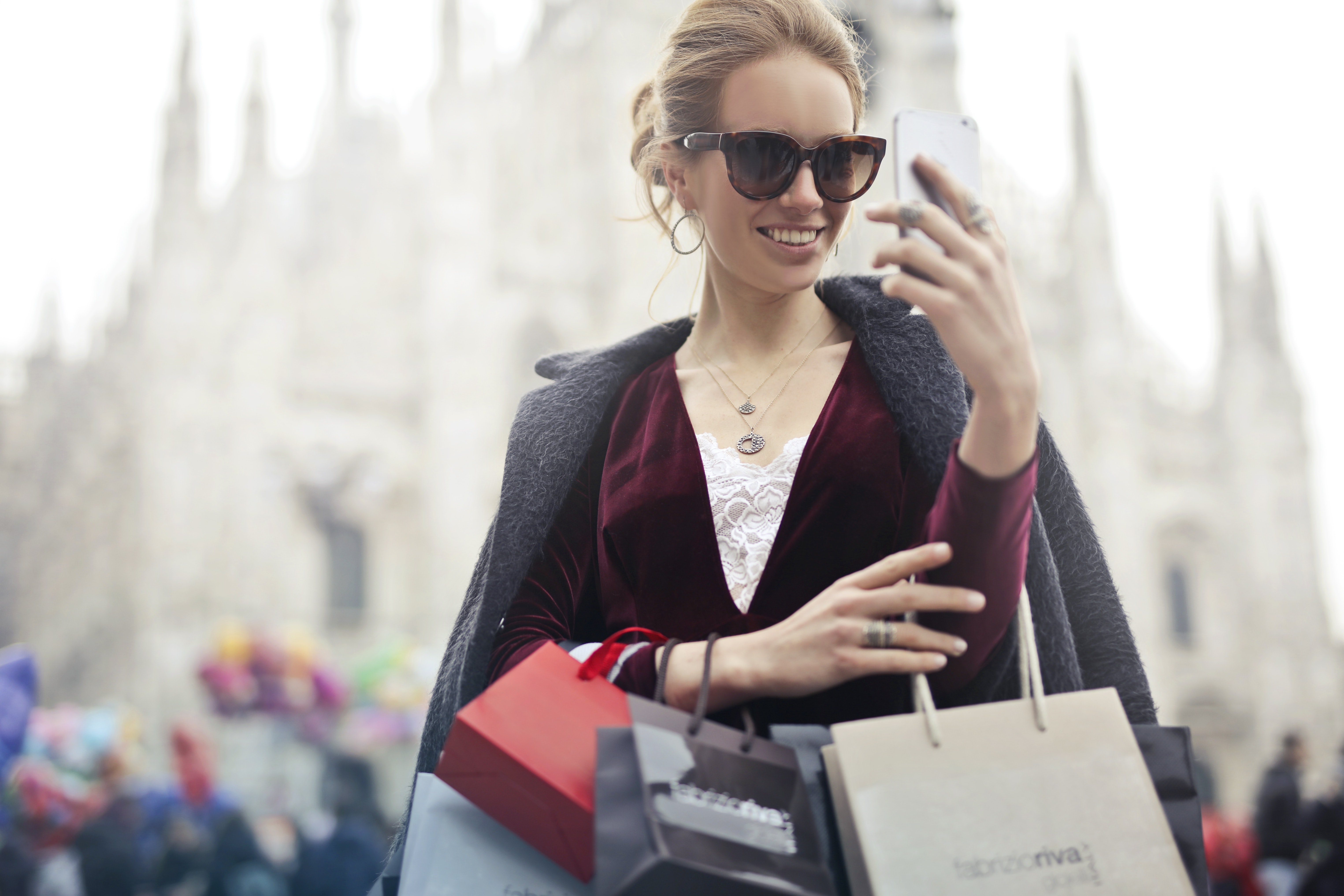 Woman in maroon long-sleeved top holding smartphone with shopping bags at daytime photo