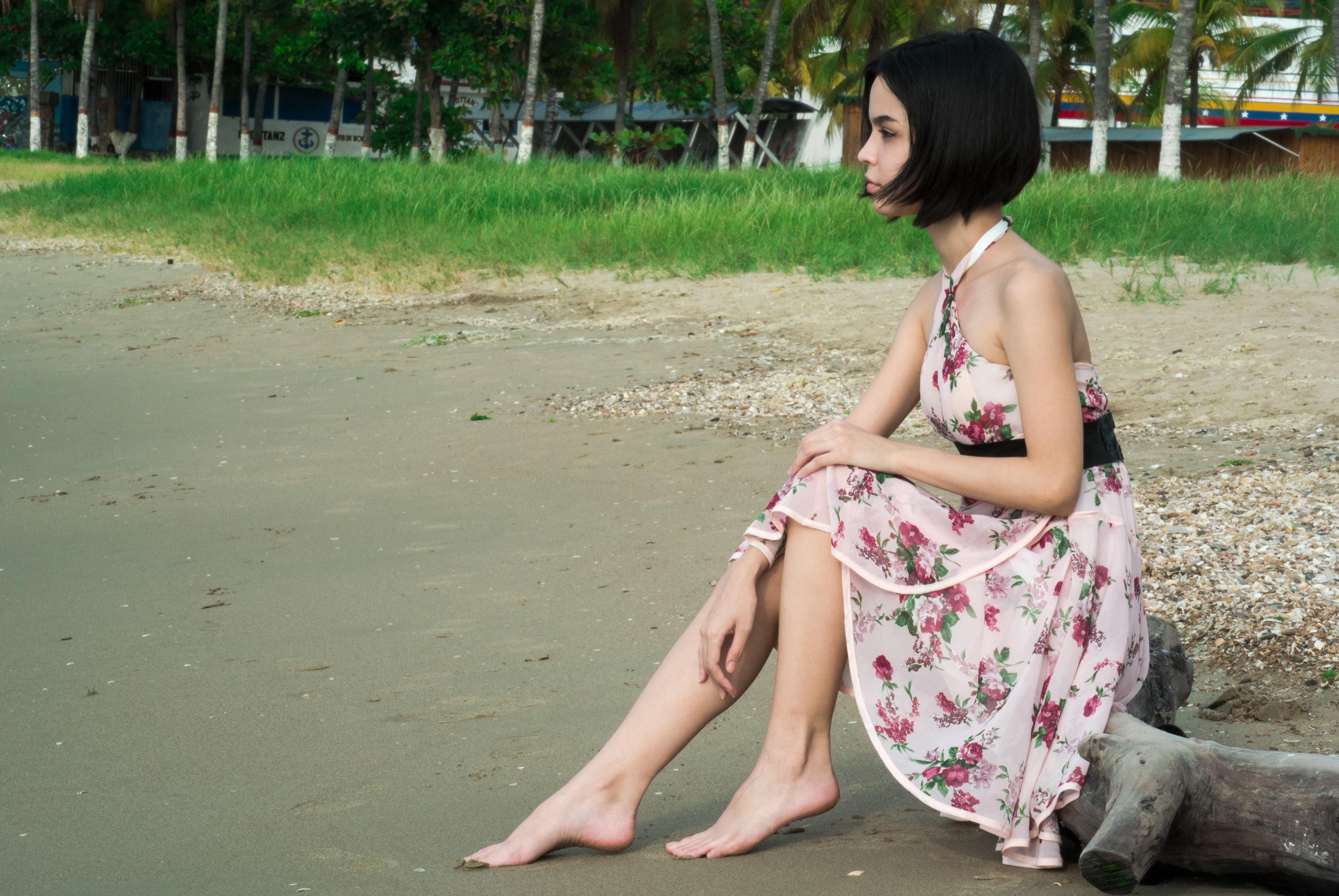 Woman in pink floral halter dress seating in driftwood photo