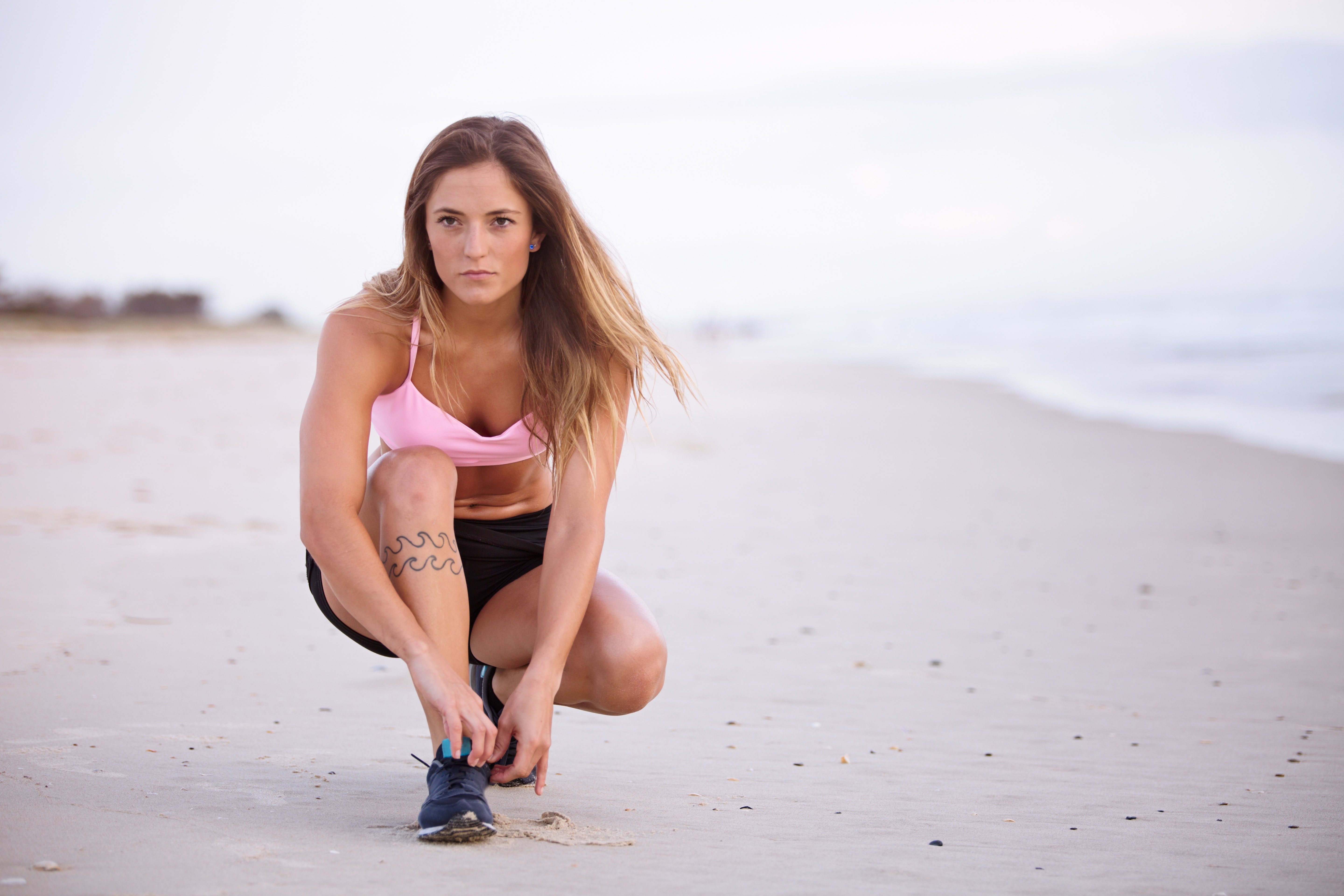 Woman in pink top and black shorts lacing her shoes on sea shore photo