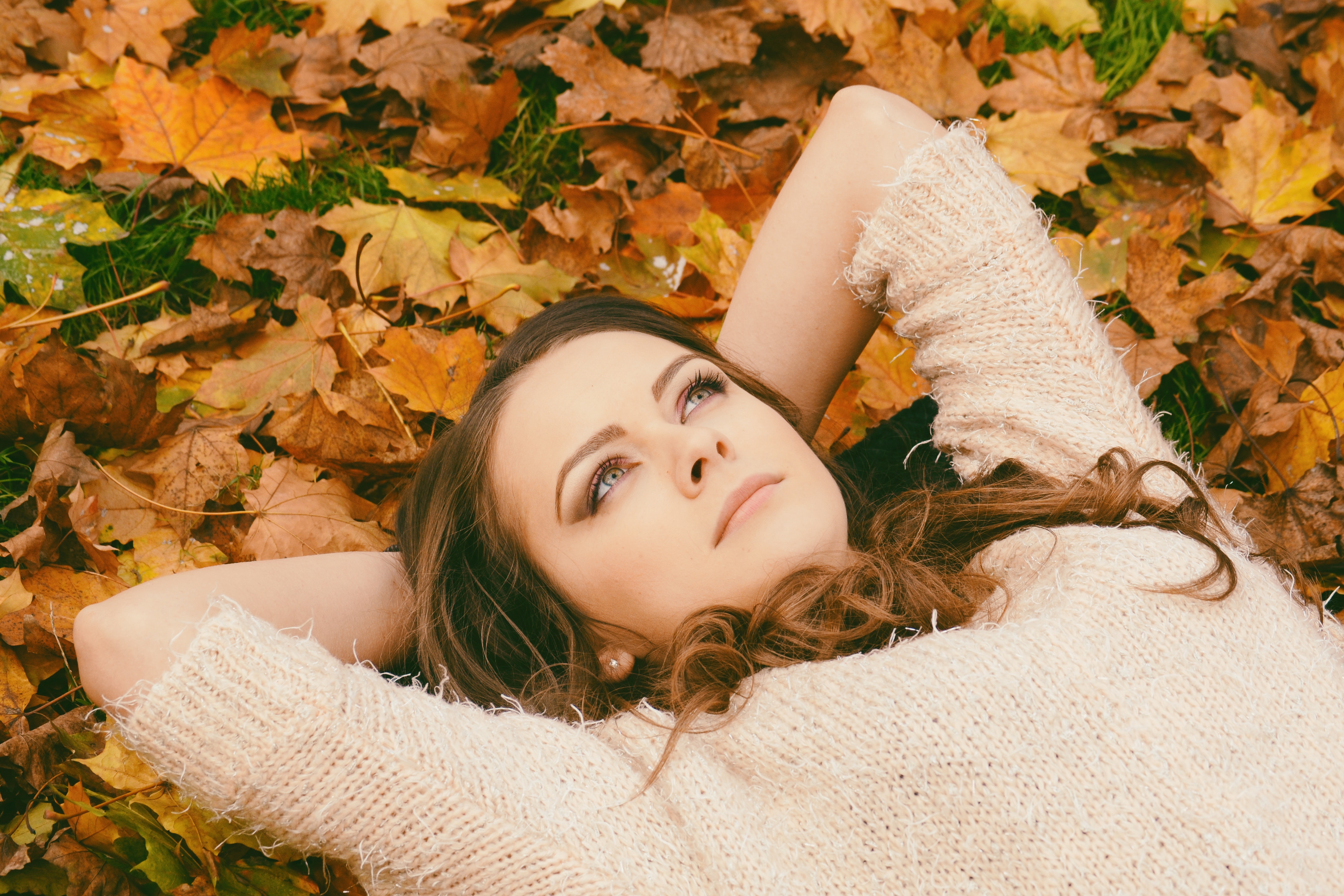 Woman in sweater laying on dried maple leaves photo
