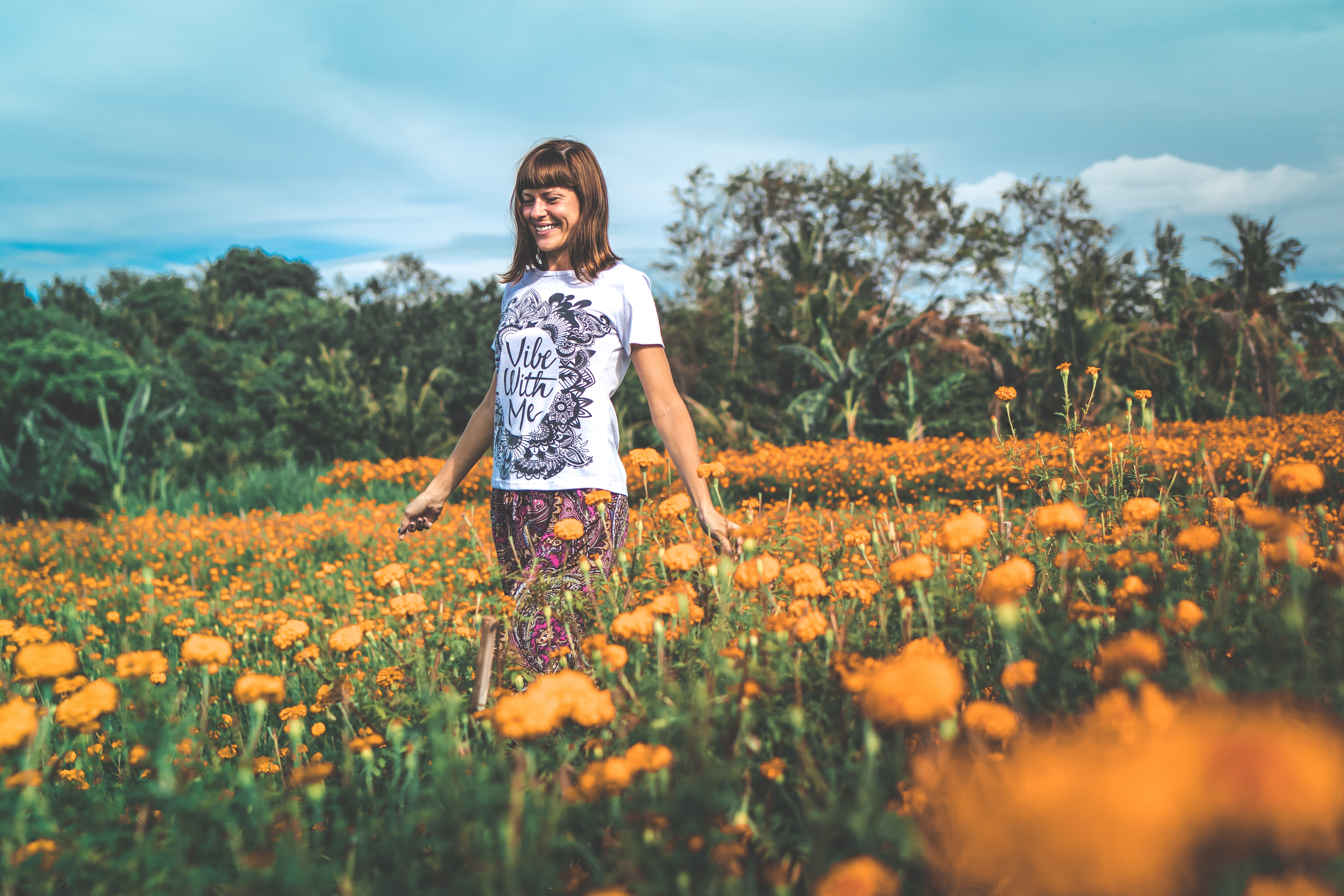 Woman in white and black floral crew-neck t-shirt and red bottoms standing on orange petaled flower field at daytime photo