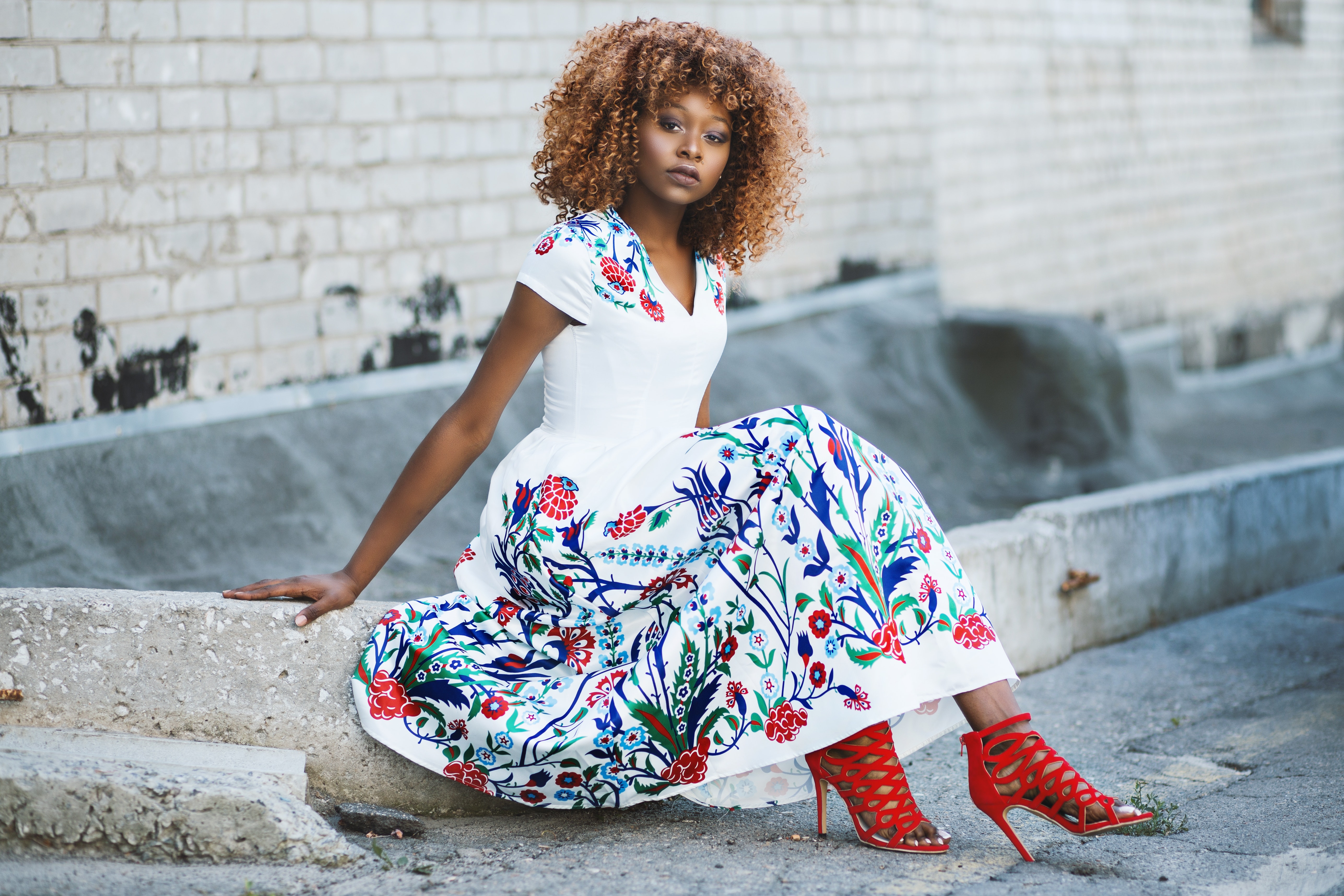 Woman in white and multicolored floral flare dress sitting on concrete photo