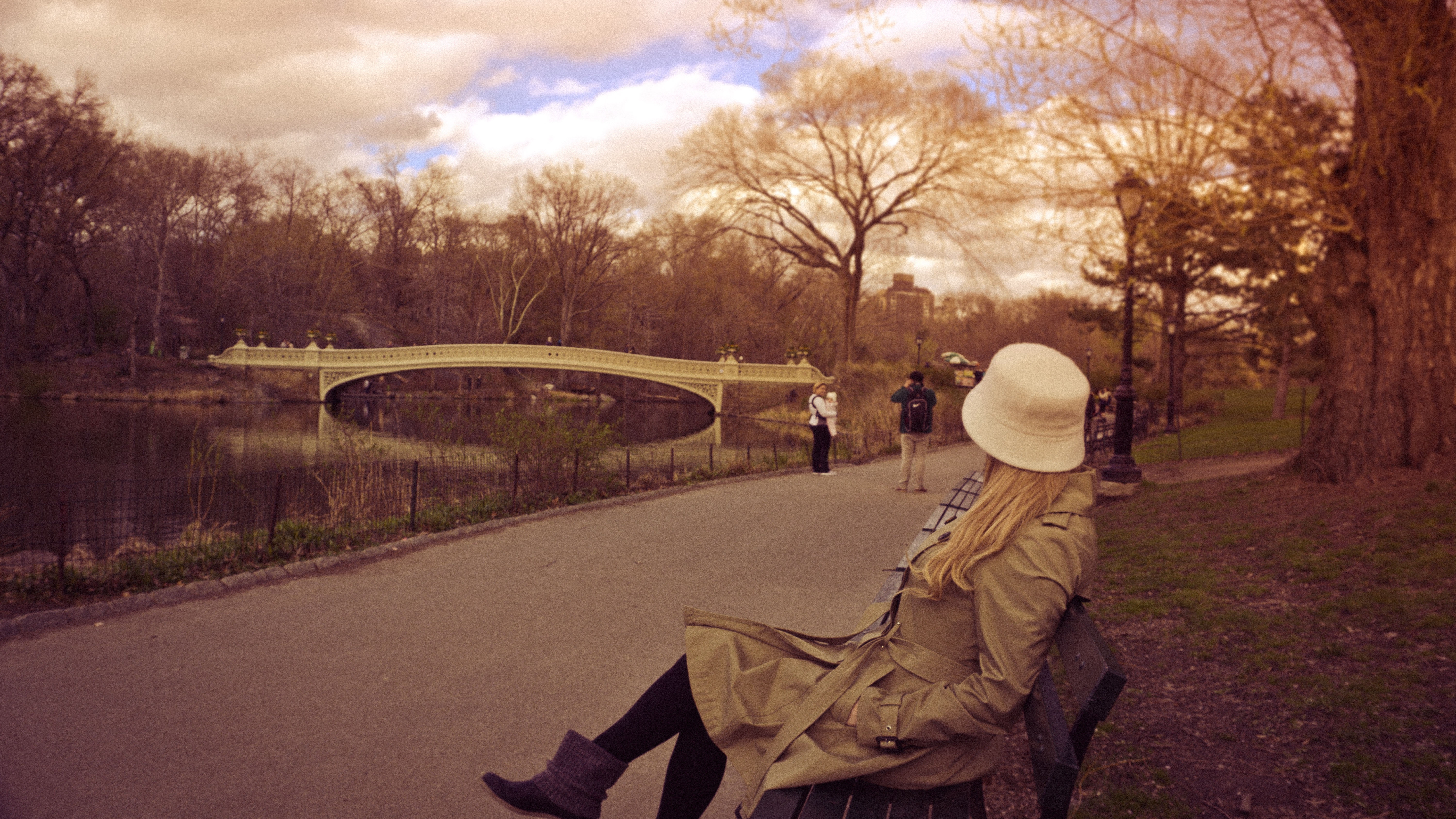 Woman in white bucket hat, brown coat and boots sitting on bench at park photo
