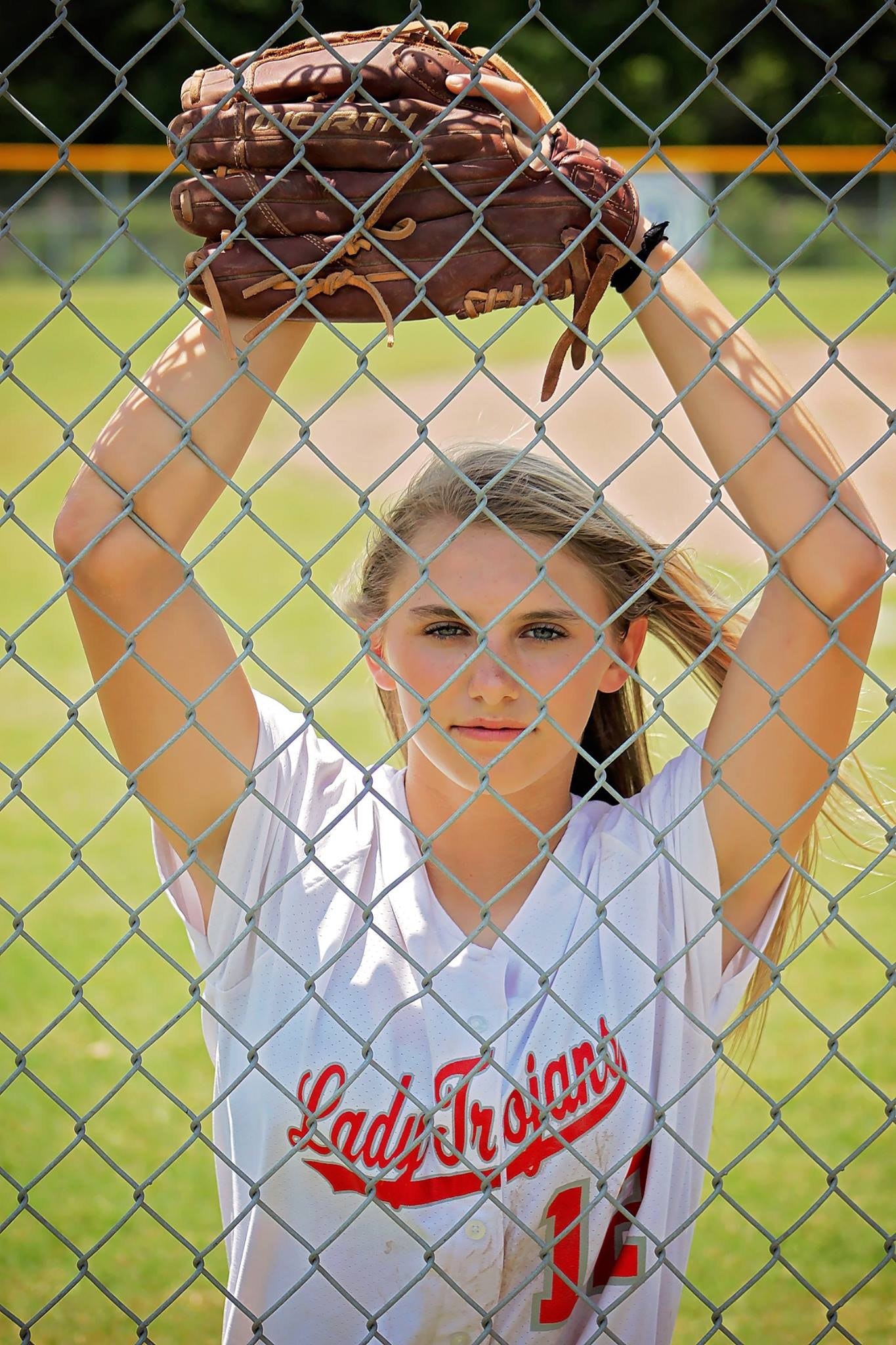 Woman in white crew neck t-shirt with baseball mitt in front of fence photo