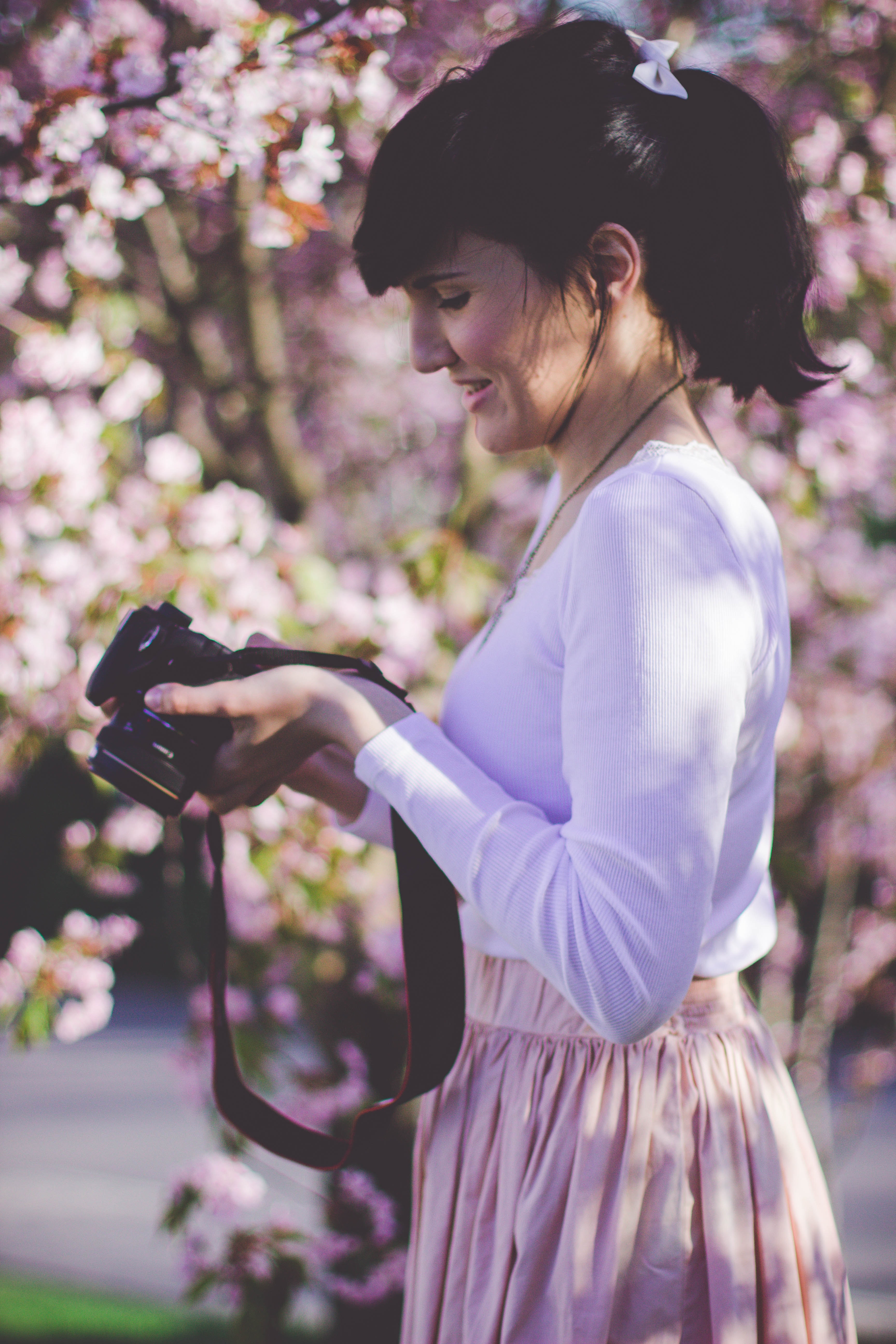 Woman in white long sleeve top and pink skirt holding black dslr camera photo