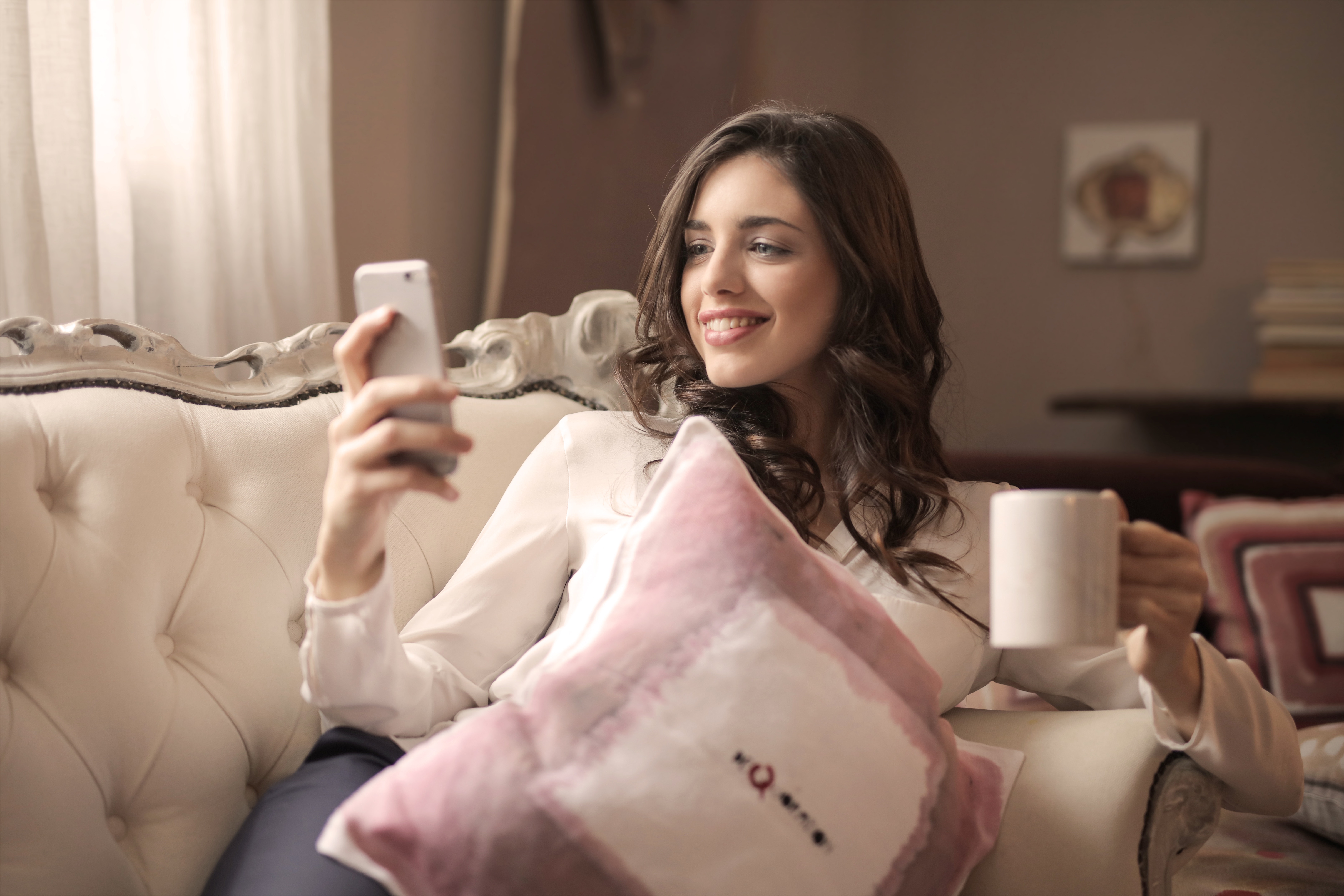 Woman in white long-sleeved shirt holding smartphone sitting on tufted sofa photo