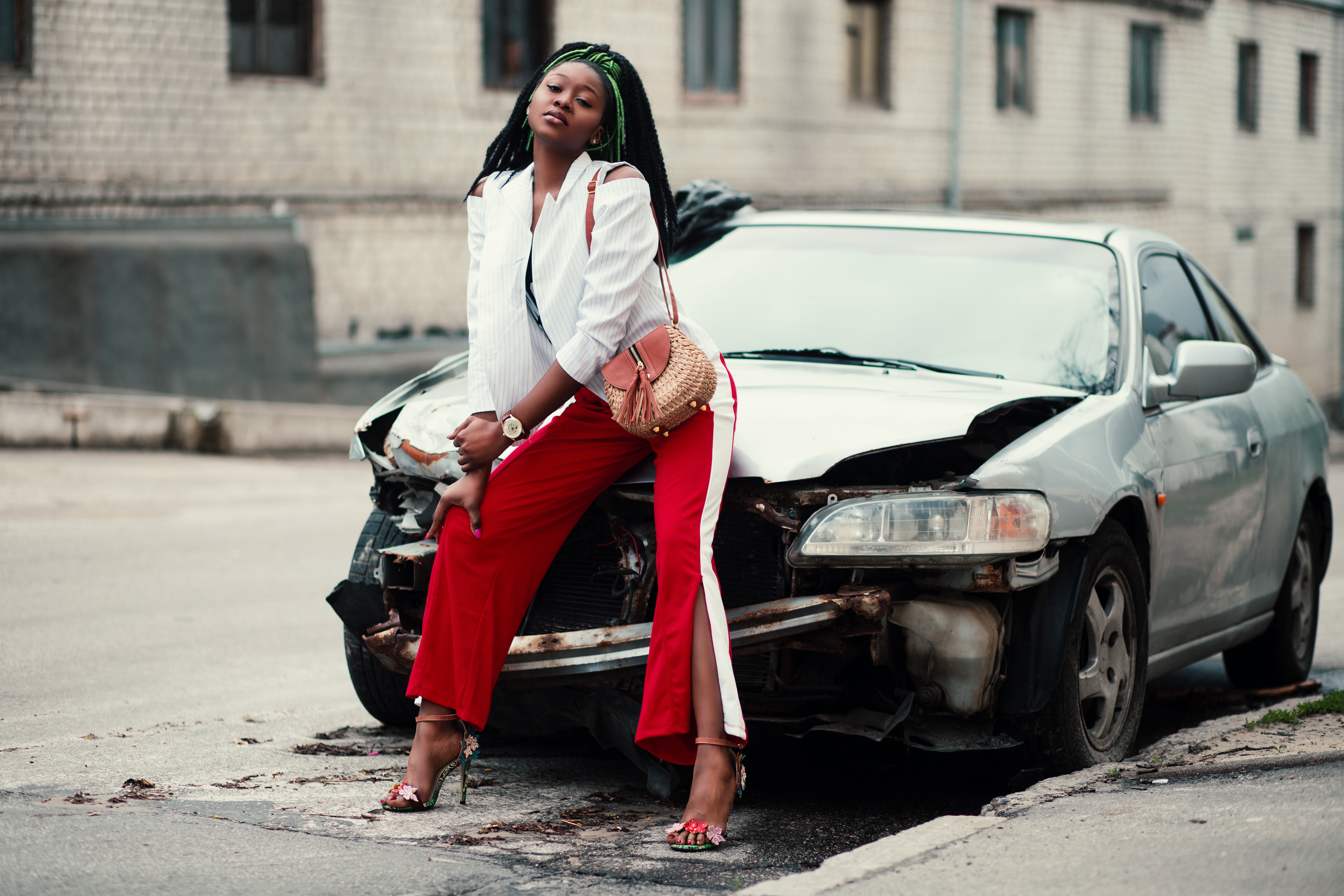 Woman in white open cardigan and red and white pants sitting on damage white car photo
