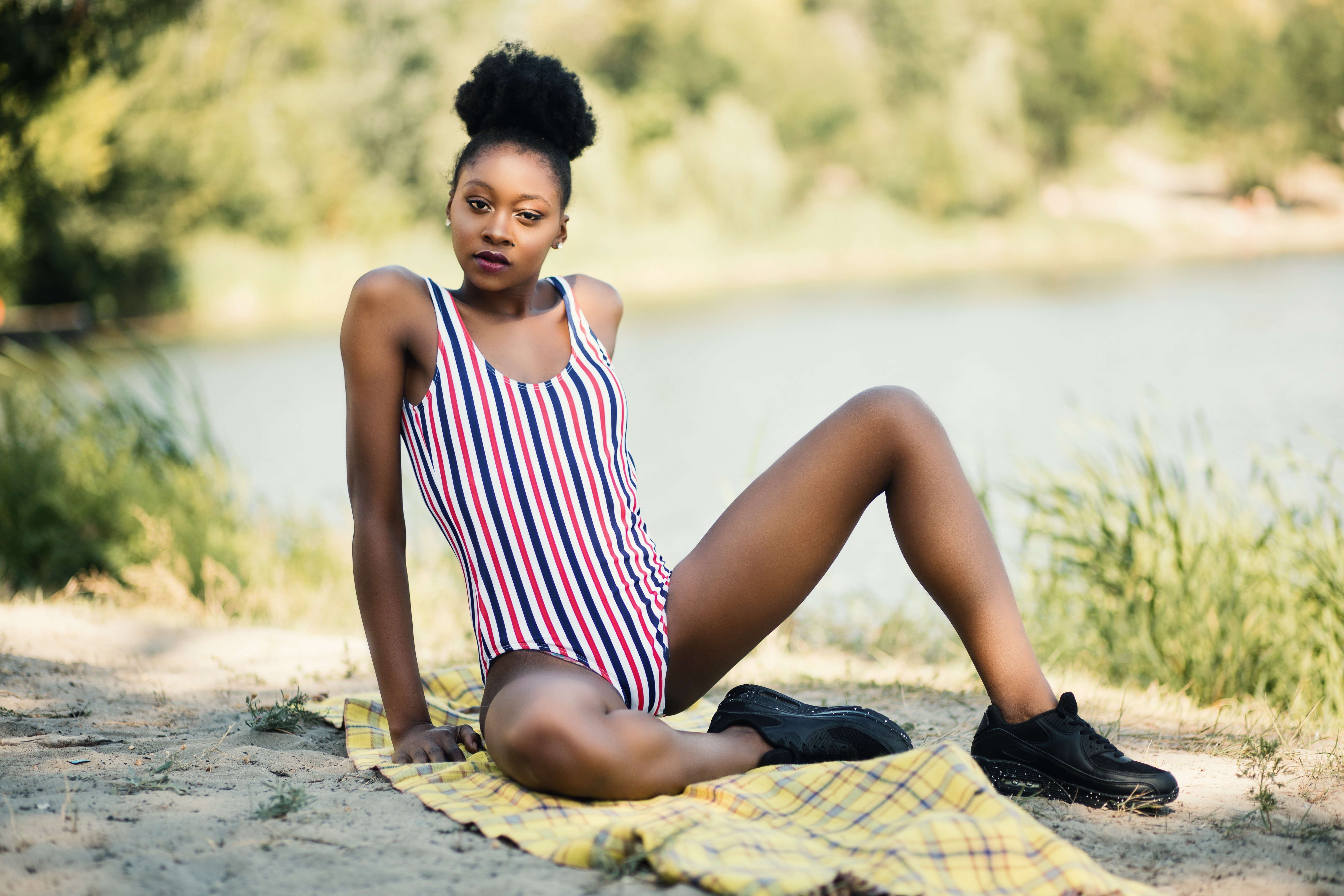 Woman in white, red, and blue striped one-piece suit sitting near river photo