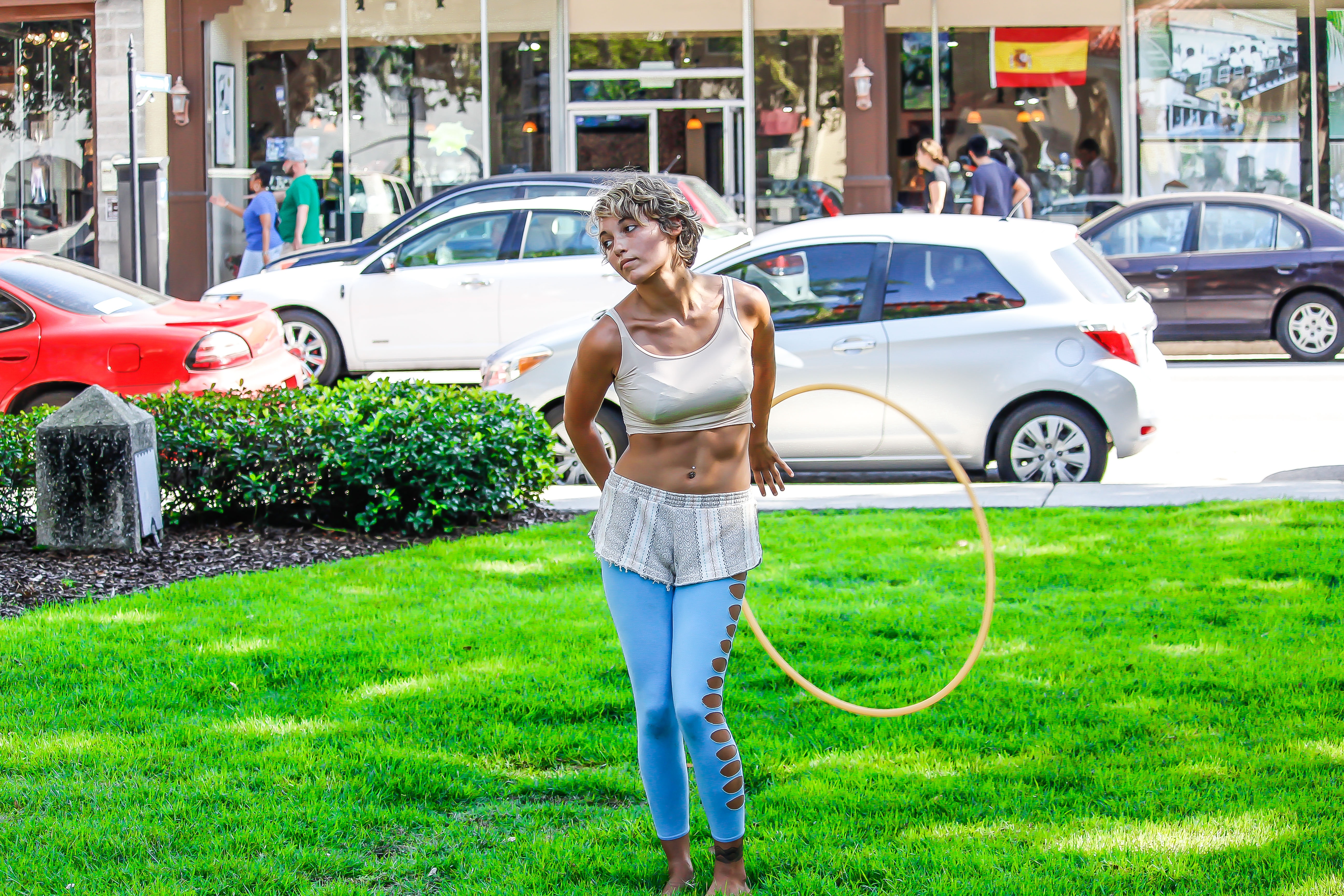 Woman in white sleeveless shirt and blue pants holds yellow hula hoop stands on green grass photo