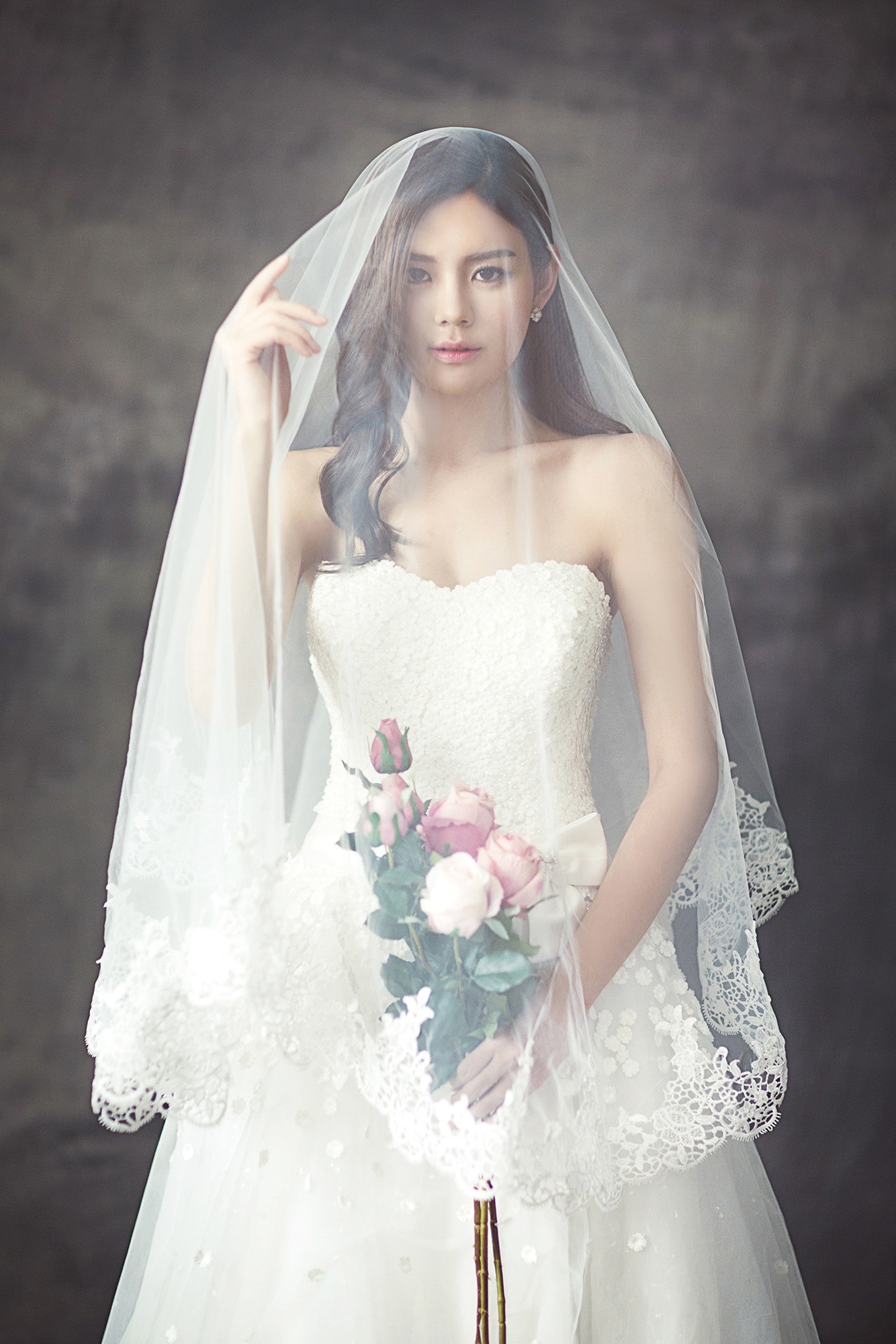 Woman in white strapless sweetheart wedding dress with rose bouquet covered in white veil photo
