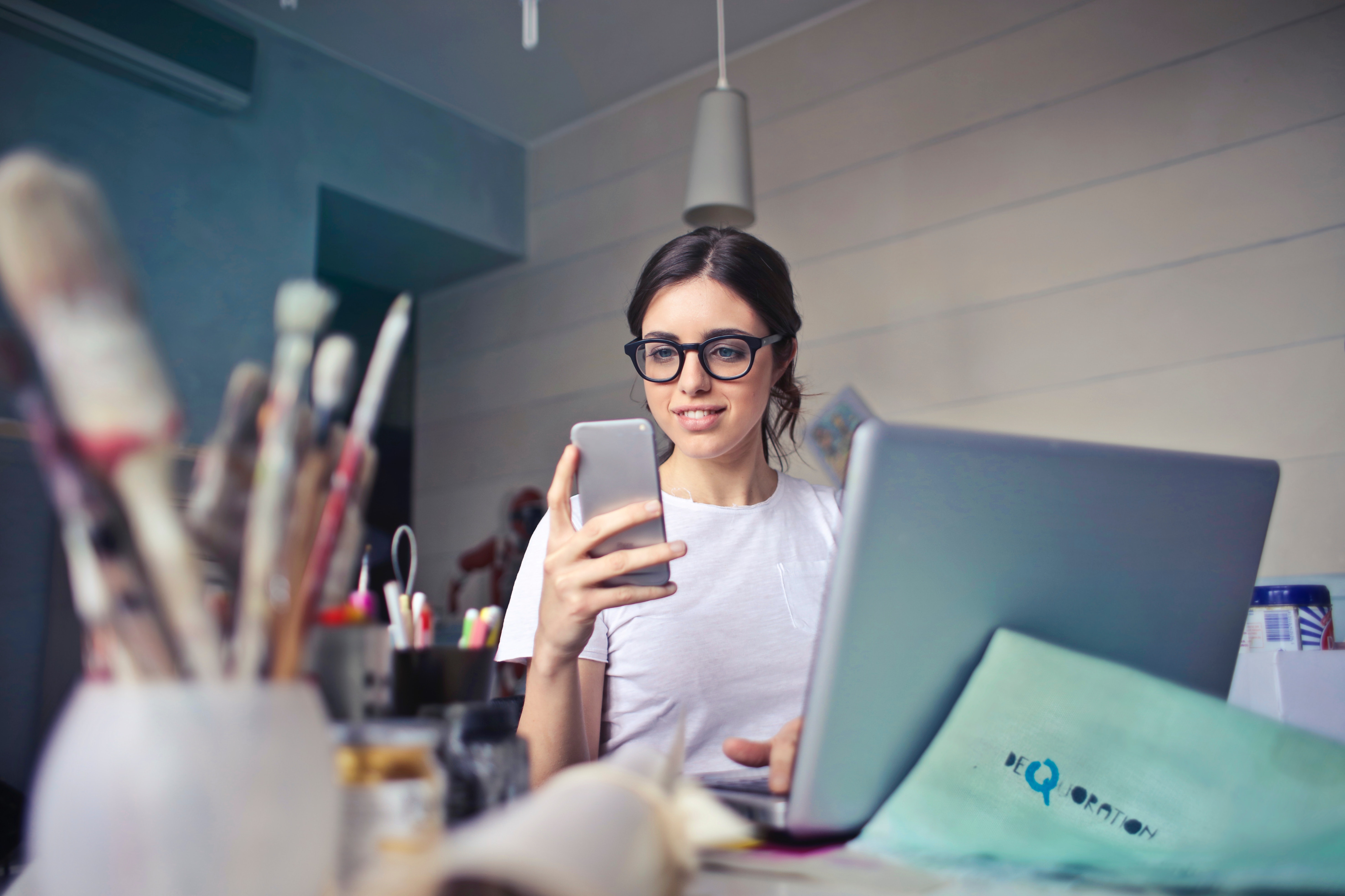 Woman in white t-shirt holding smartphone in front of laptop photo