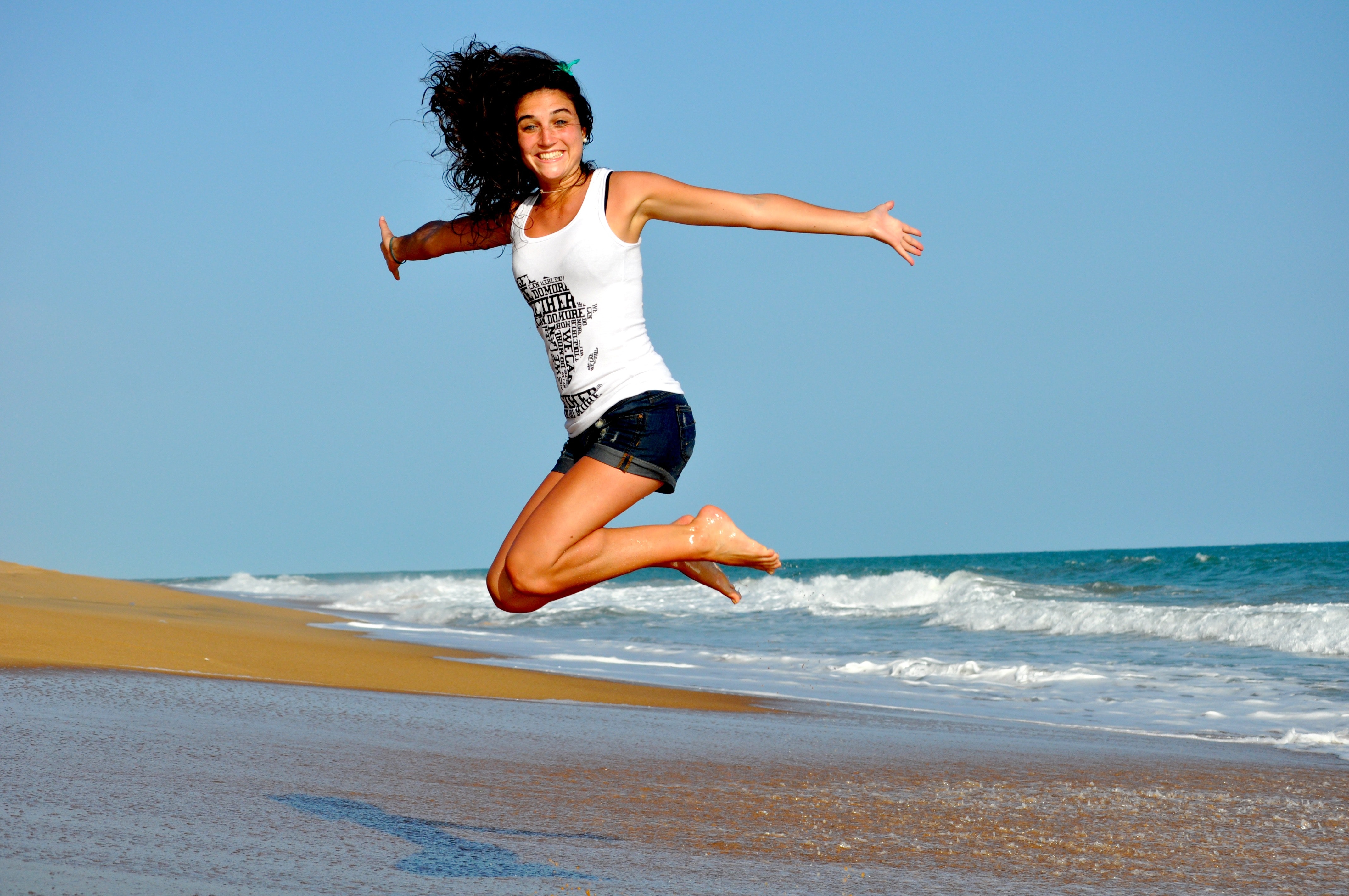 Woman in white tanktop jump over beach sand photo