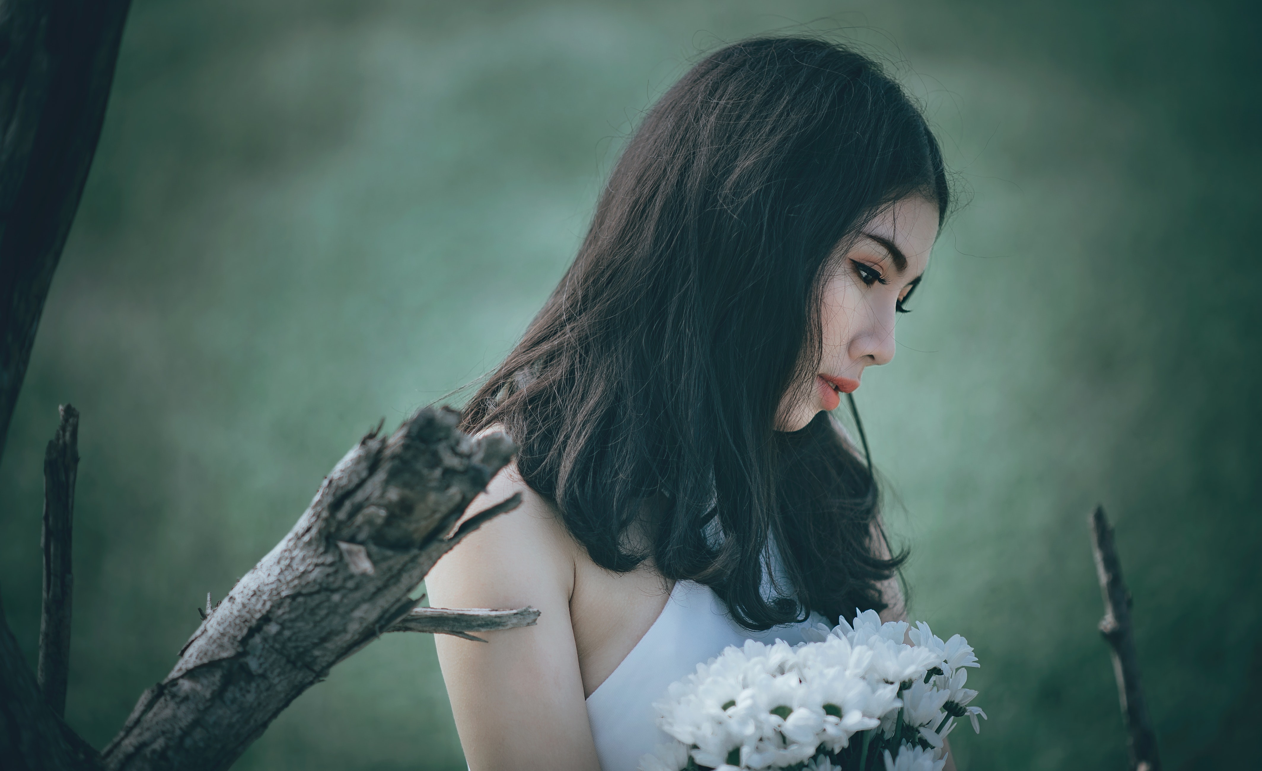 Woman in white top holding bouquet of white petaled flowers while looking down photo