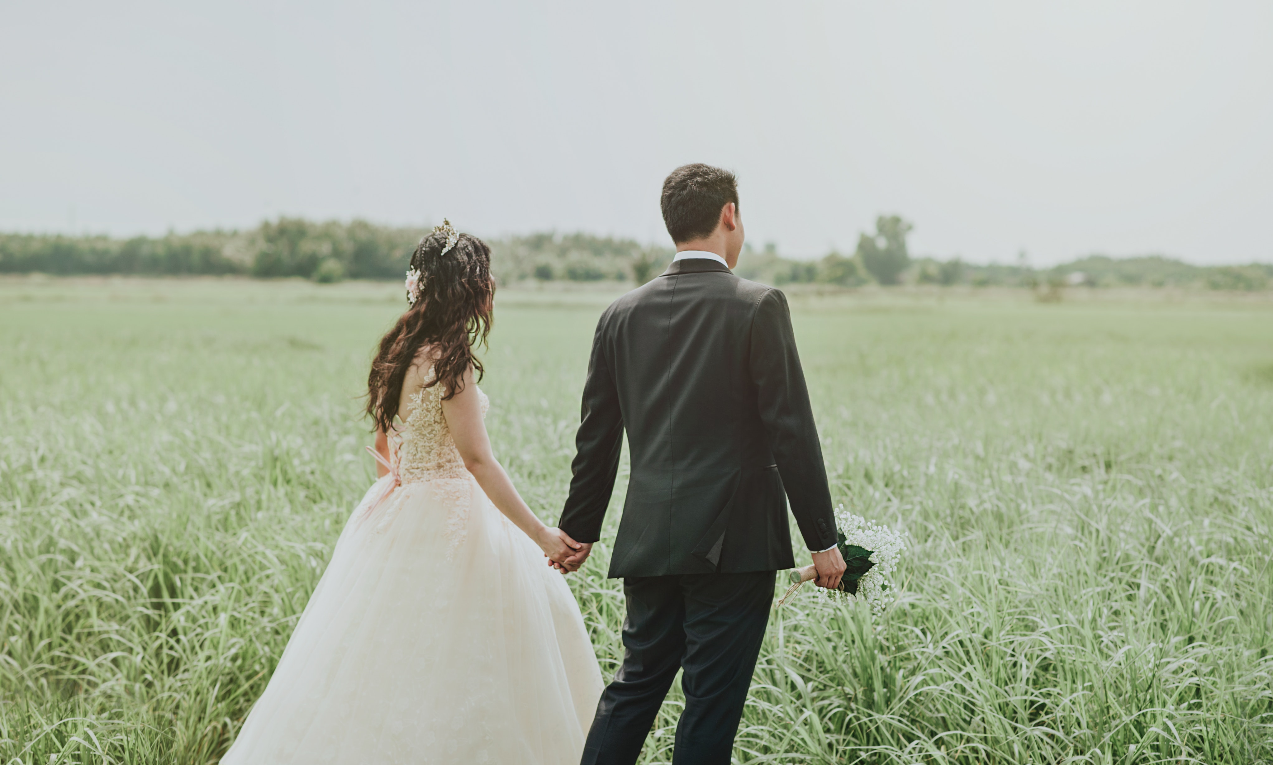Woman in white wedding dress holding hand to man in black suit photo