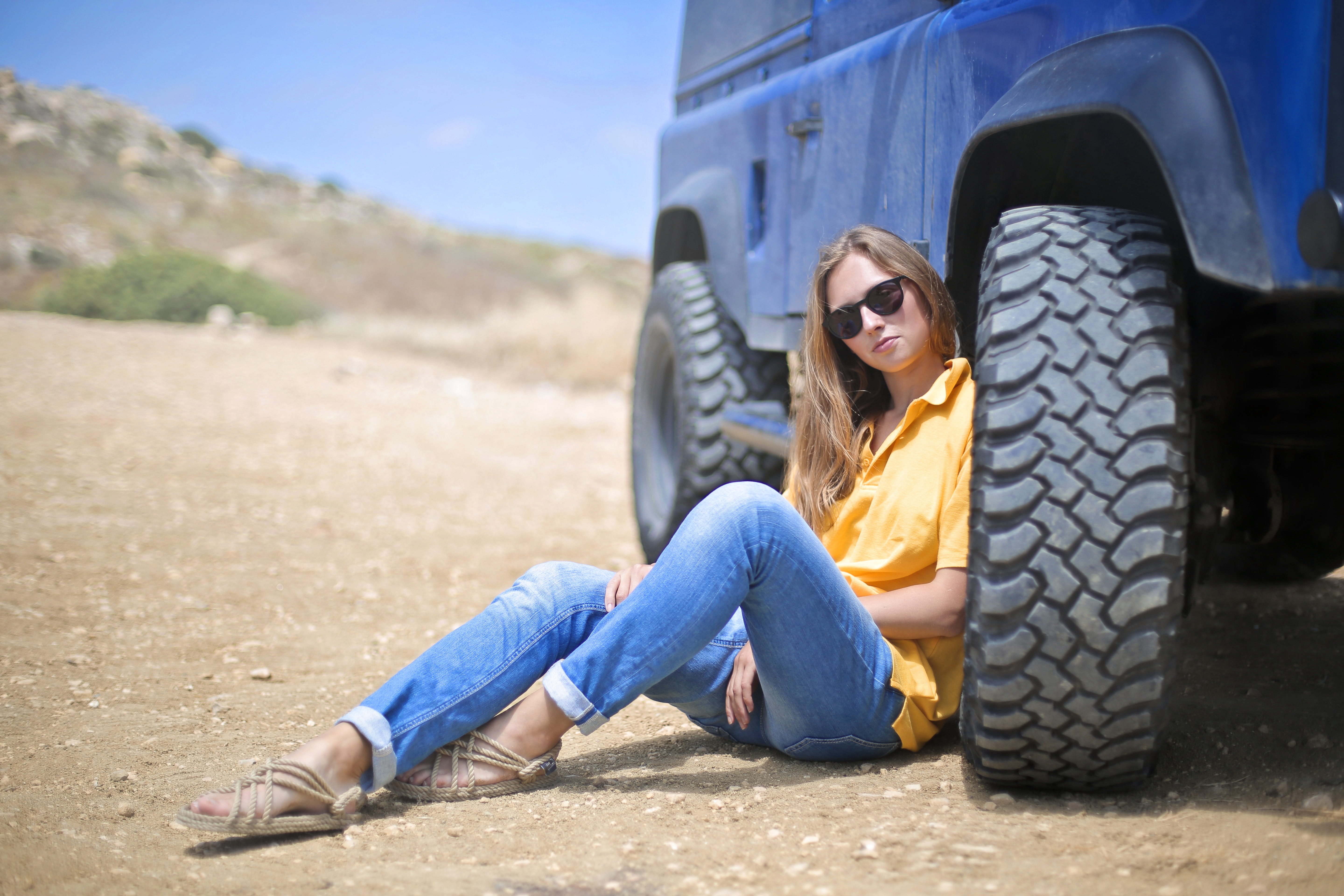 Woman in yellow polo shirt sitting on ground leaning on blue vehicle at daytime photo