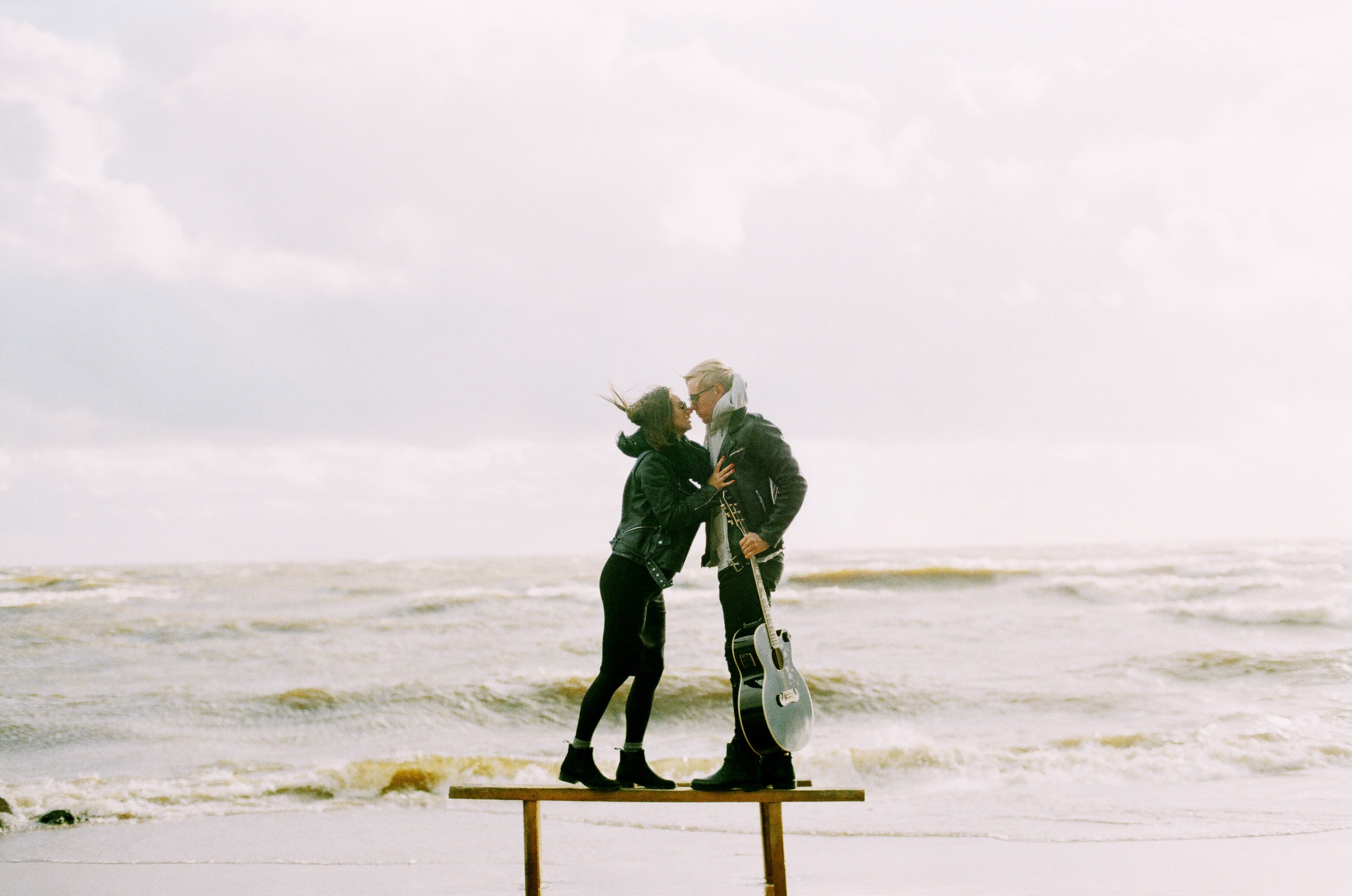 Woman kissing man holding guitar beside beach photo