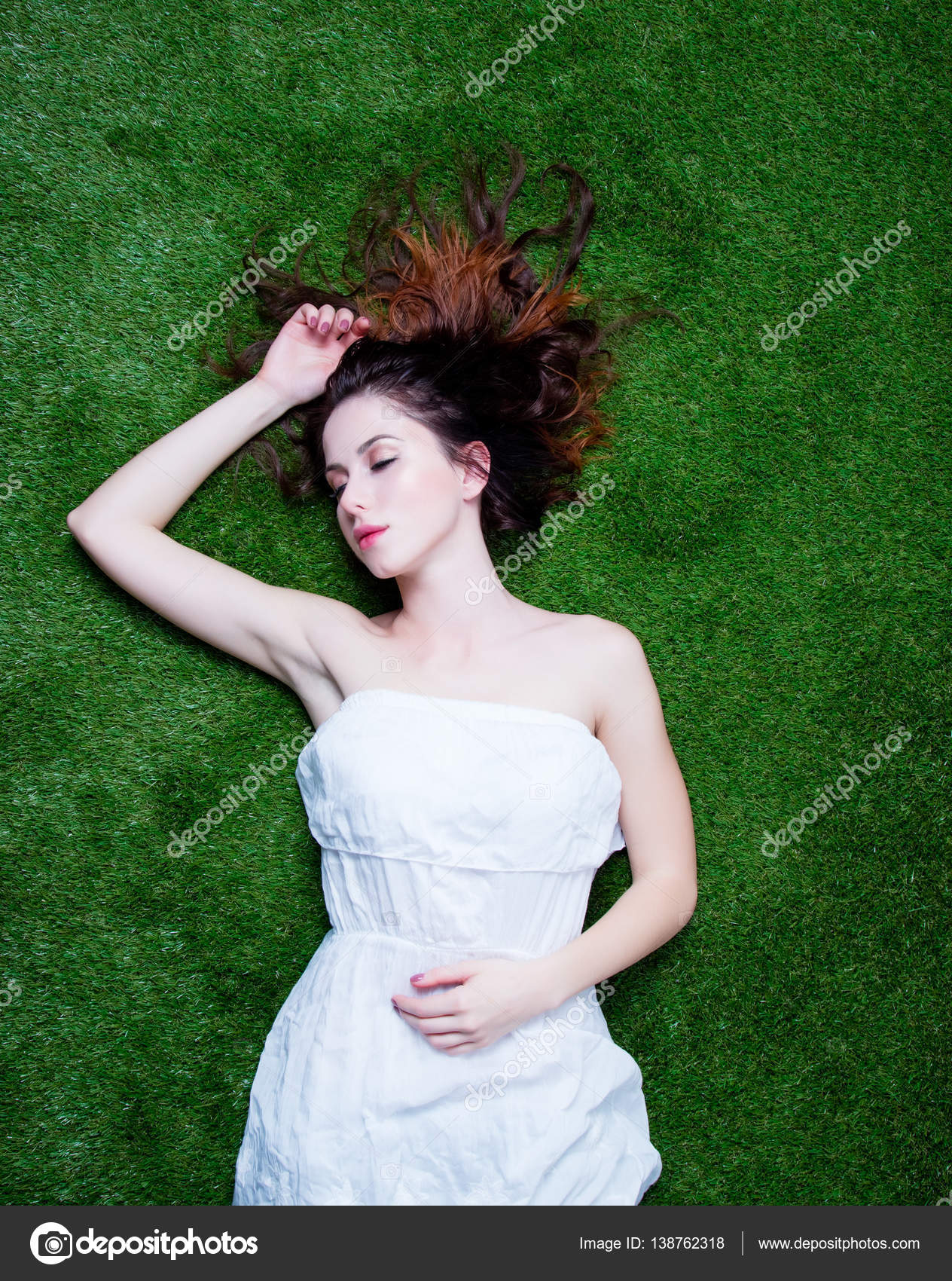 Portrait of a young redhead woman lying down on green spring gra ...