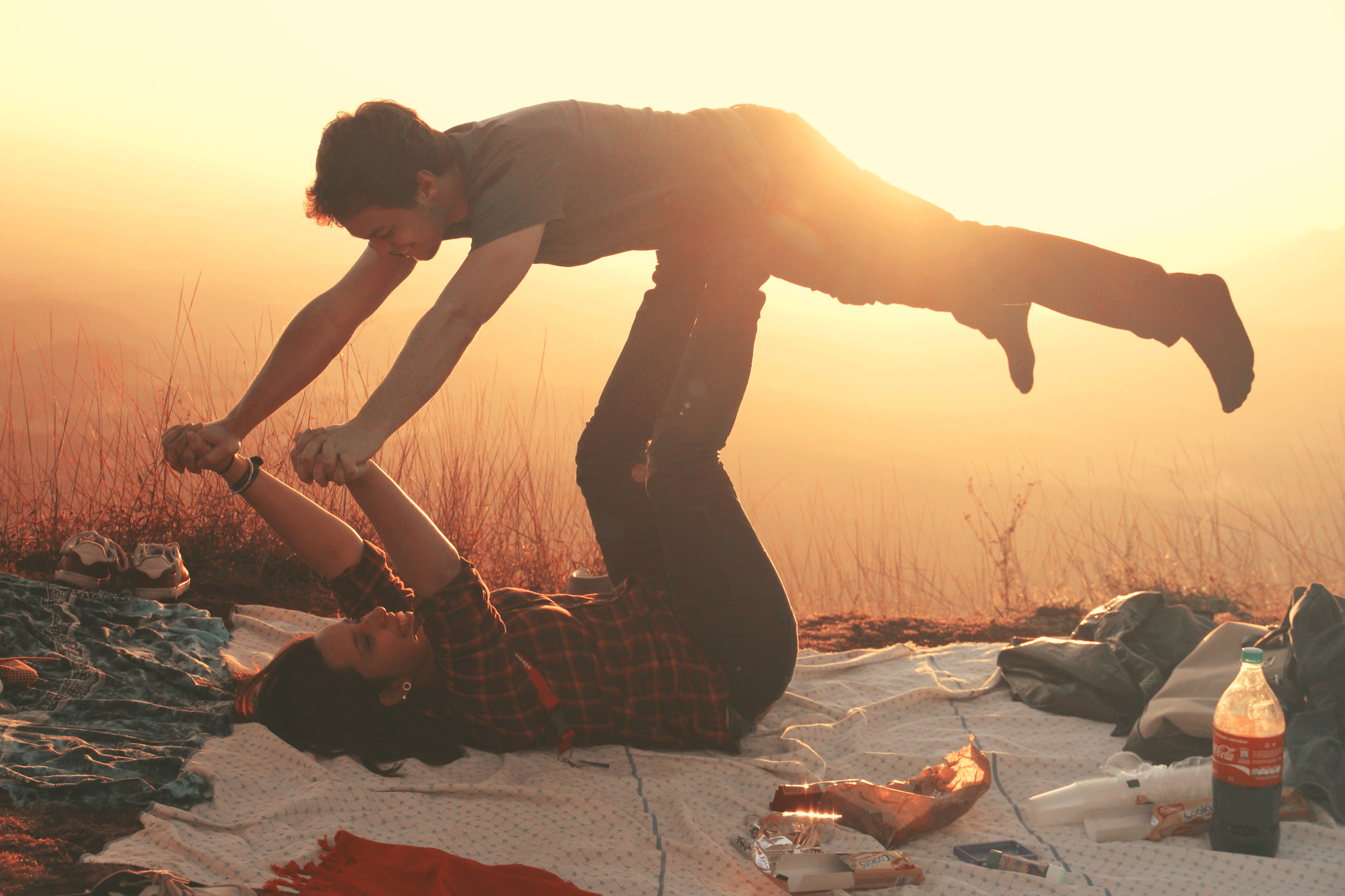 Woman lying on blanket under man on her legs holding hands during golden hour photo