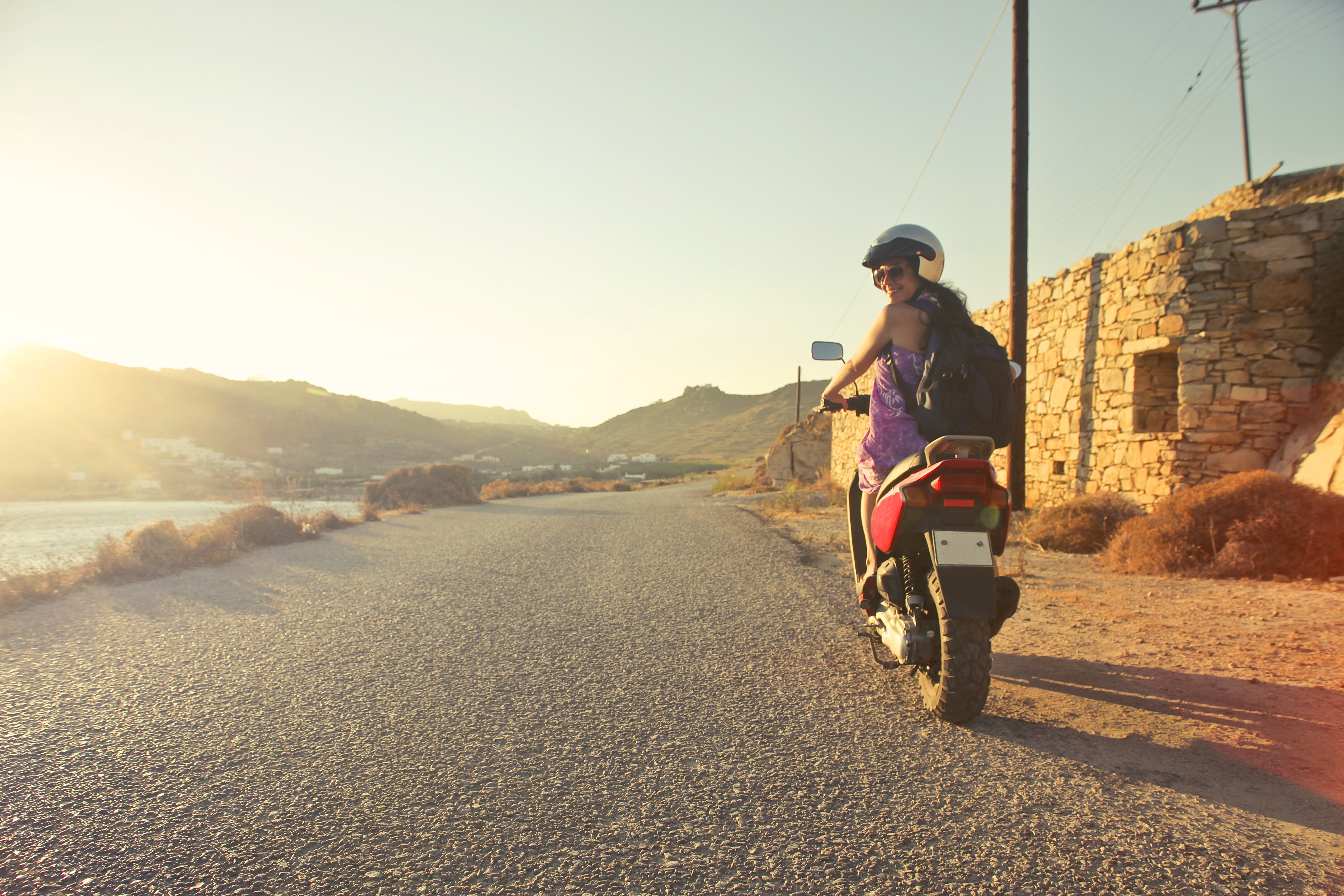 Woman riding motor scooter travelling on asphalt road during sunrise photo