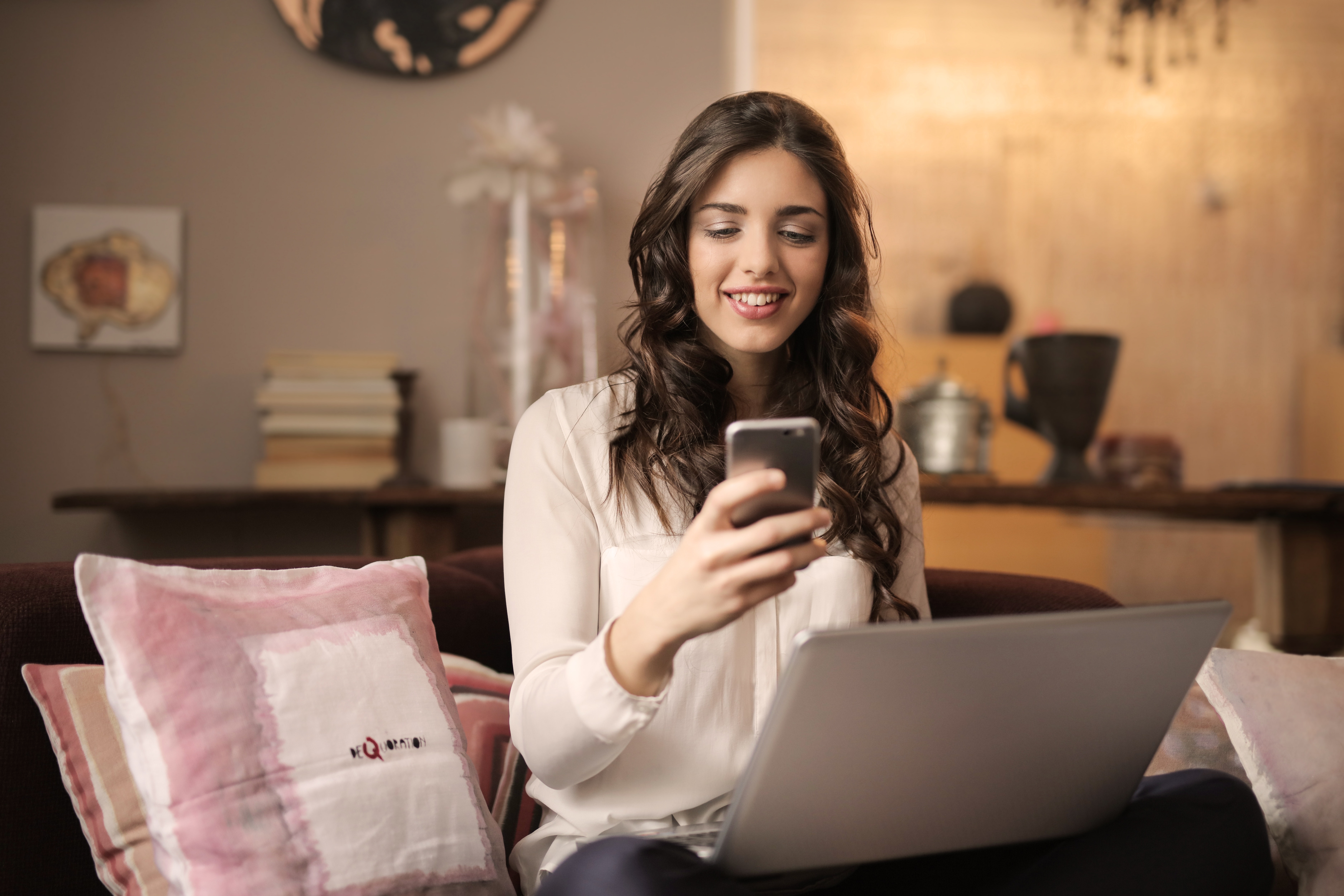 Woman sitting on sofa while looking at phone with laptop on lap photo