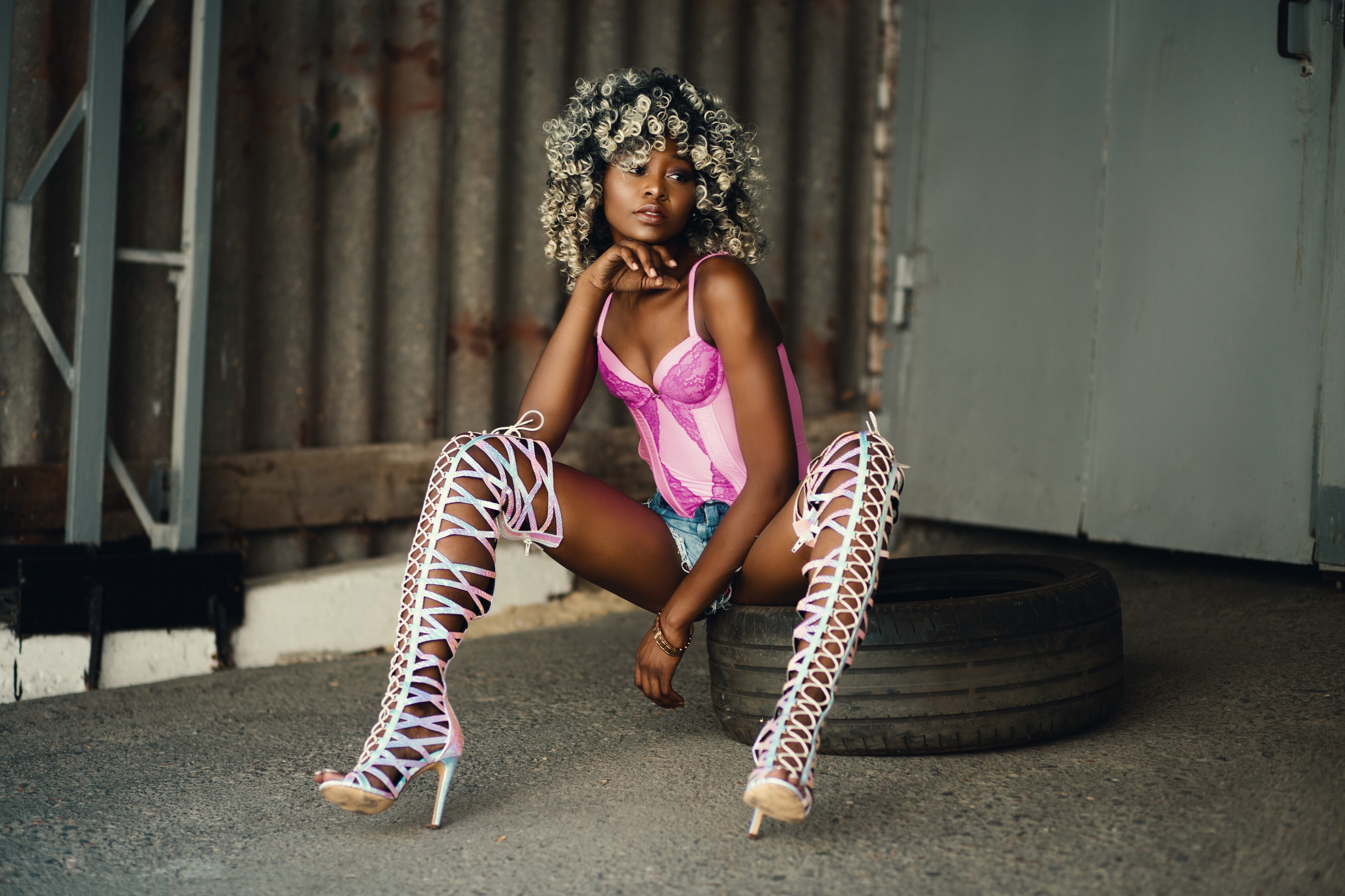 Woman sitting on vehicle tire wearing pink lingerie and white gladiator pumps photo