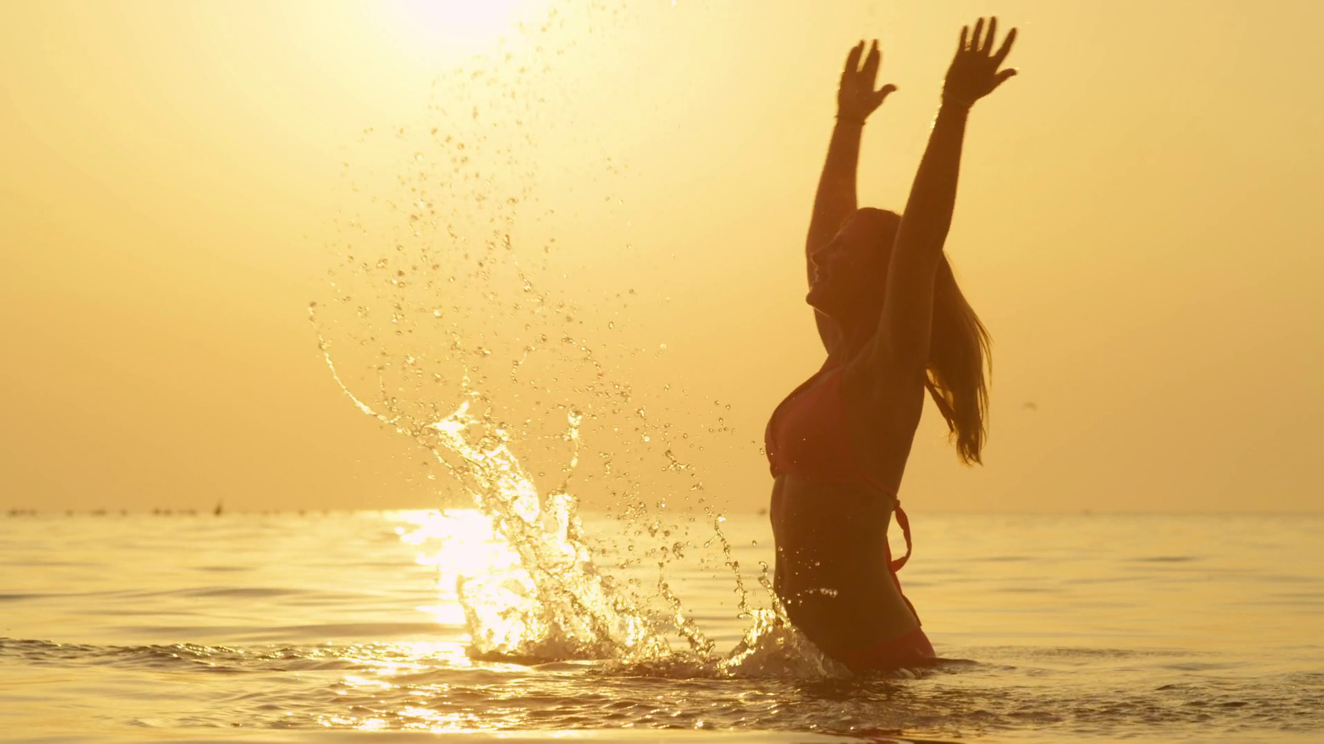 SLOW MOTION: Woman standing in ocean, raising hands up and splashing ...