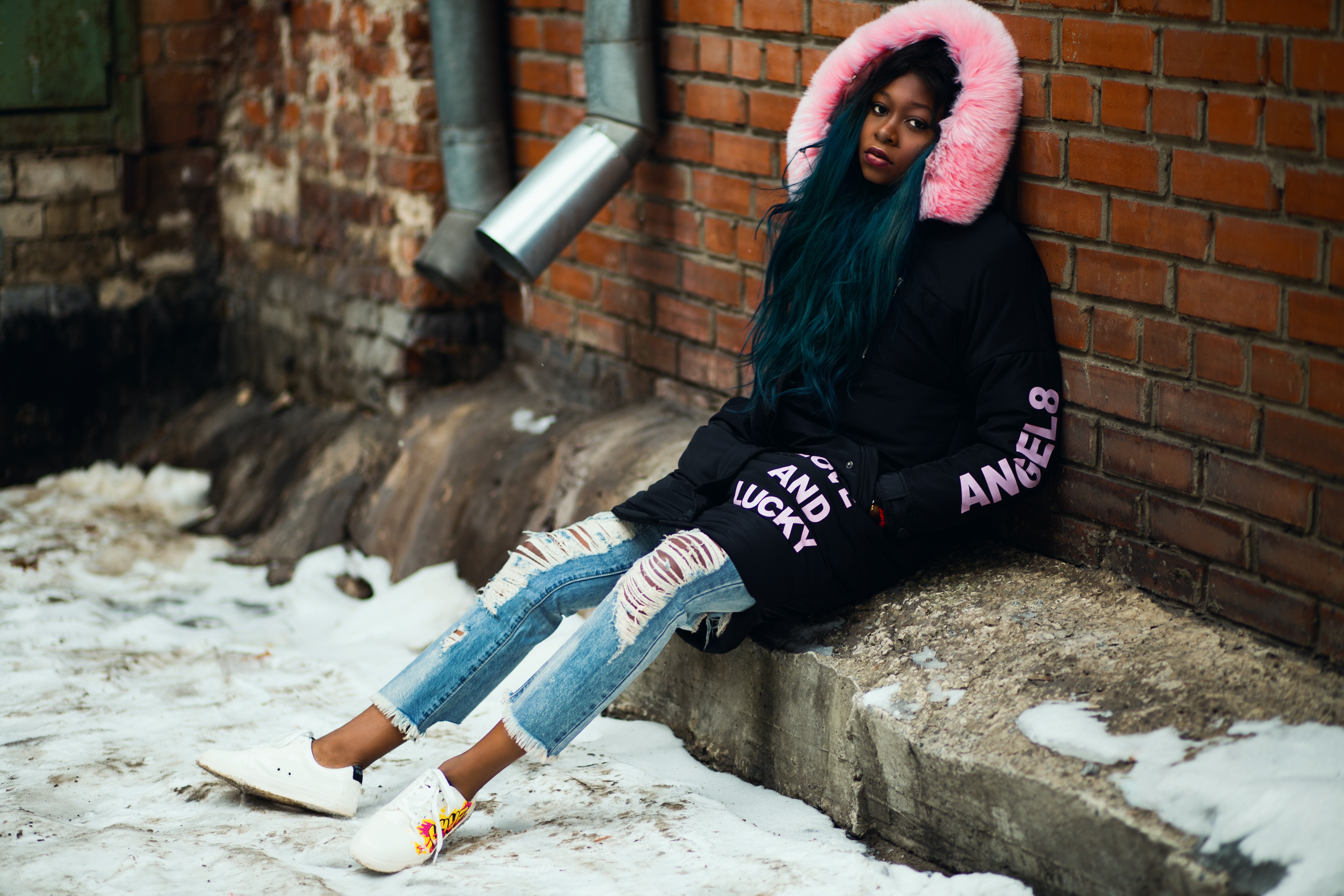 Woman wearing black and pink parka leaning on brown brick wall photo