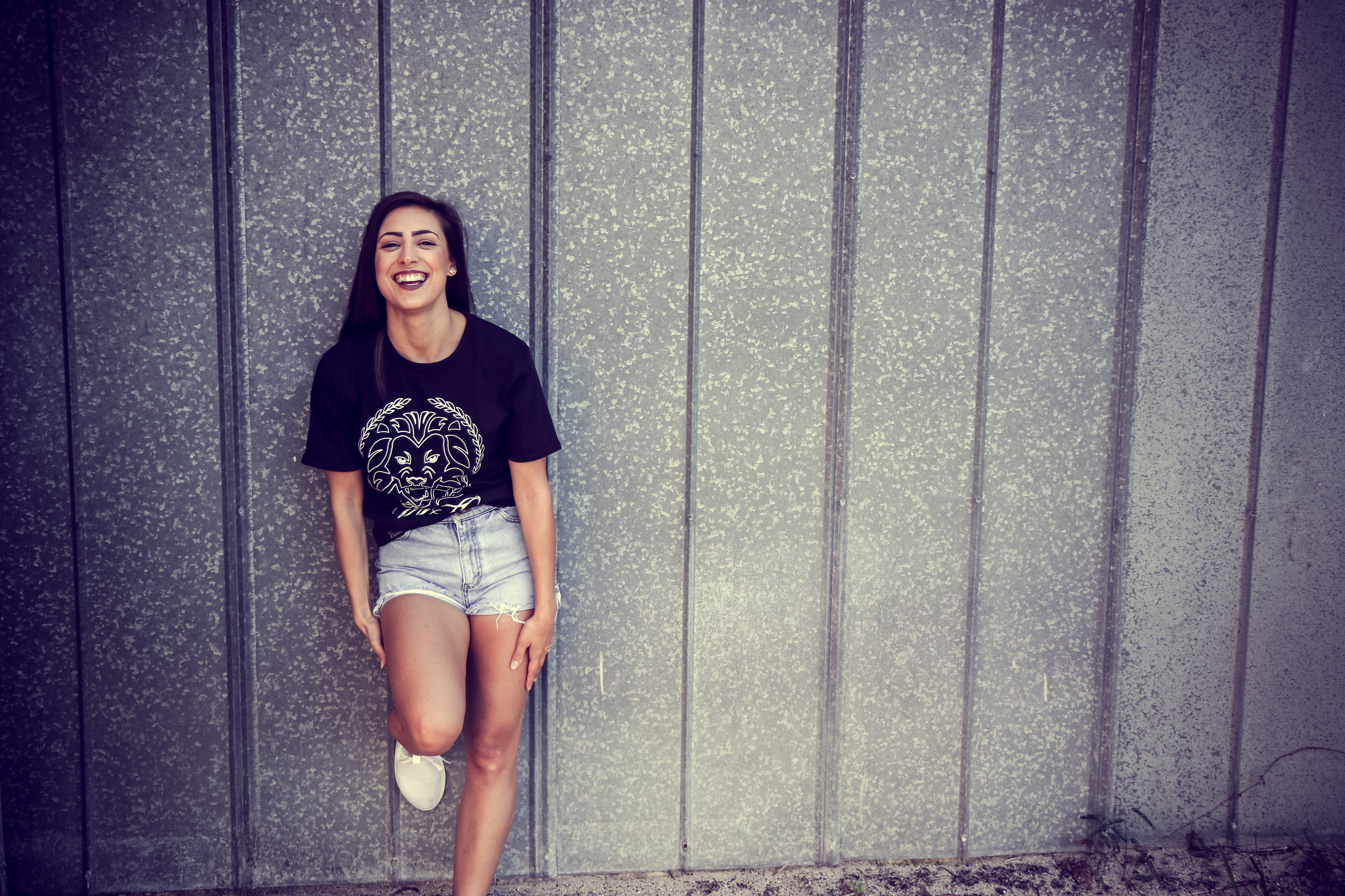 Woman wearing black and white crew-neck t-shirt and gray denim short shorts outfit leaning on gray wall photo