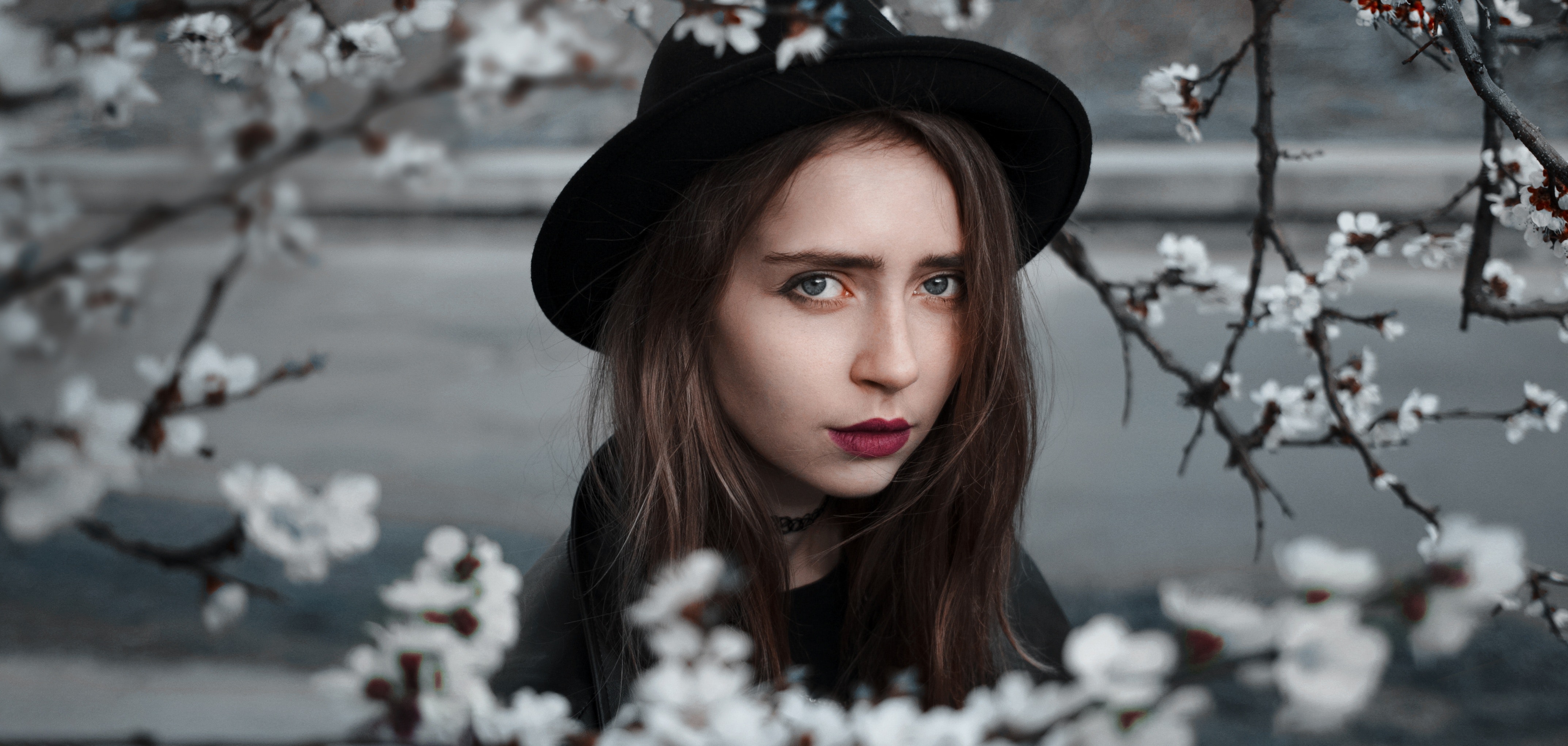 Woman wearing black hat and dress with red lipstick near white flowers selective focus photography