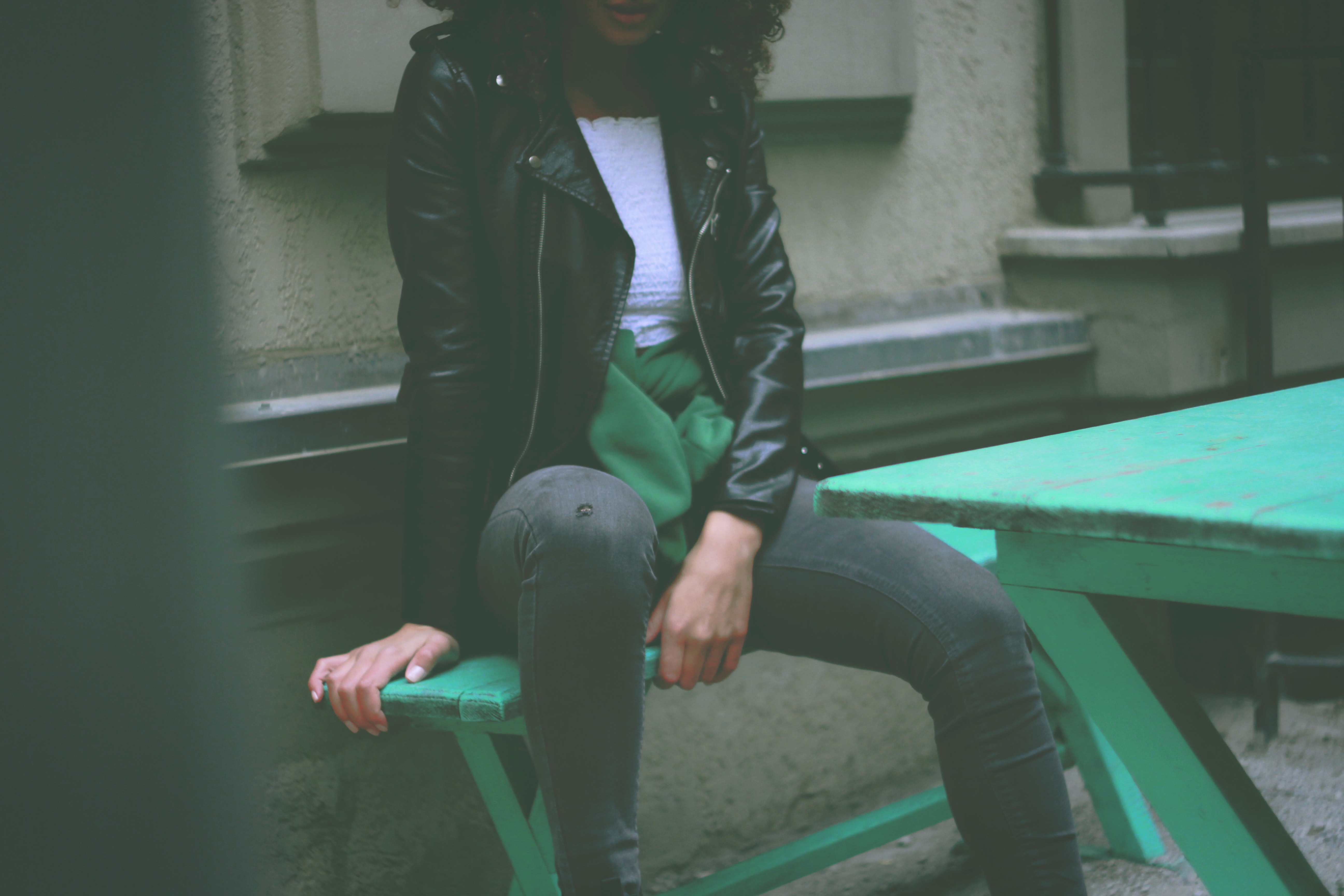 Woman wearing black leather jacket sitting on green wooden bench photo